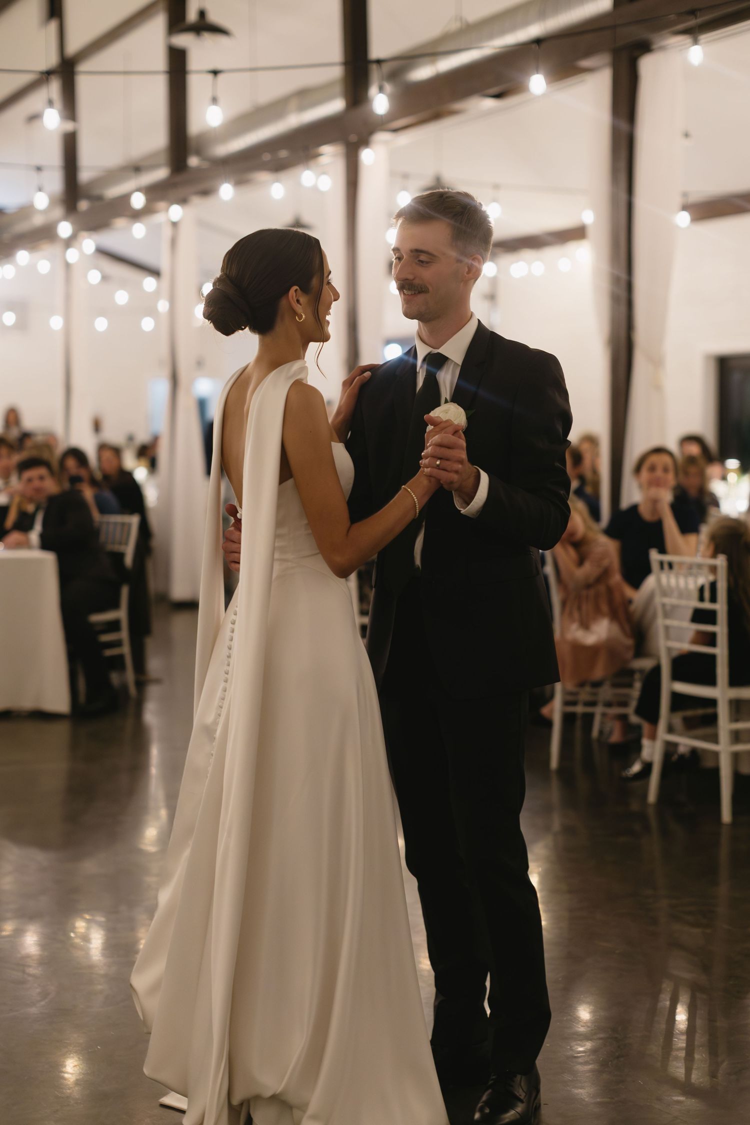 Couple shares their first dance in an elegant reception venue with string lights.