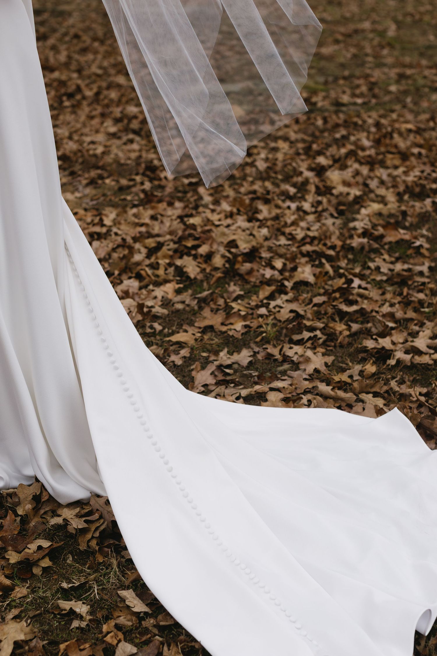 White wedding dress train with delicate buttons trailing across autumn leaves.
