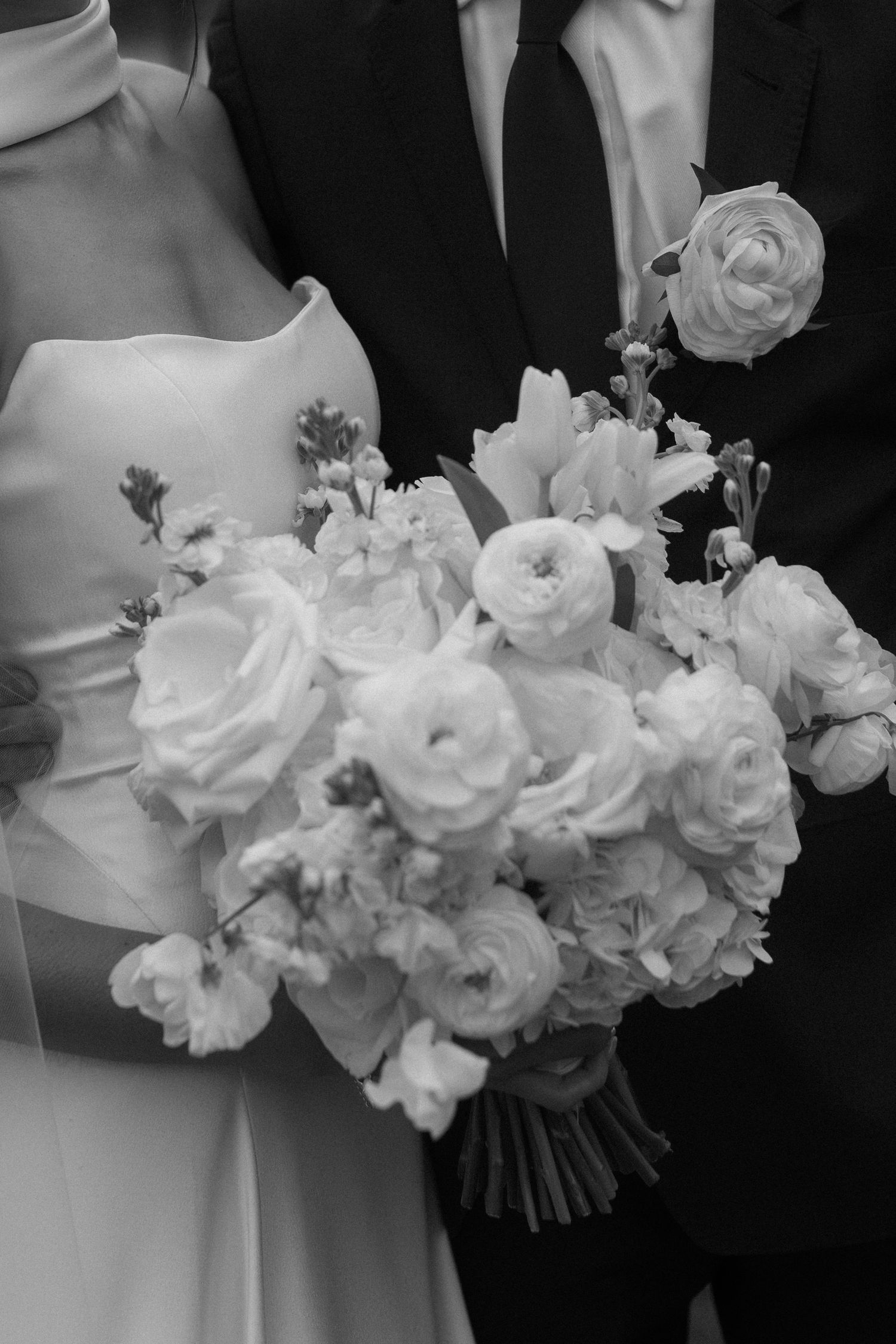 Close-up of white rose wedding bouquet against black and white formal attire.