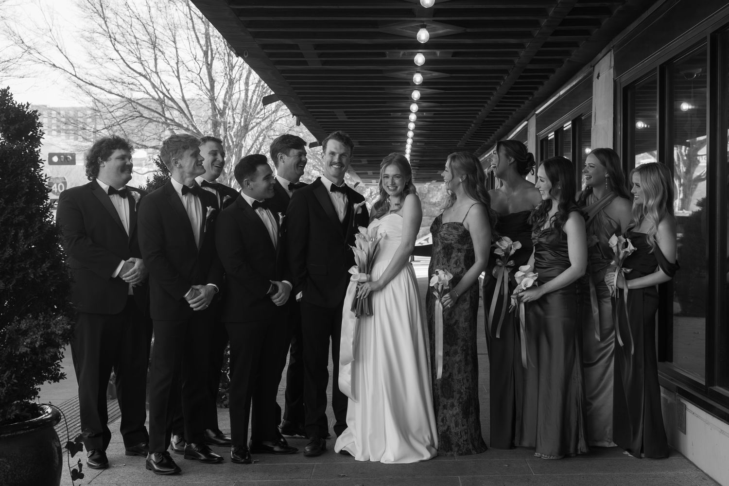 Wedding guests and party members lined up under covered walkway during celebration.