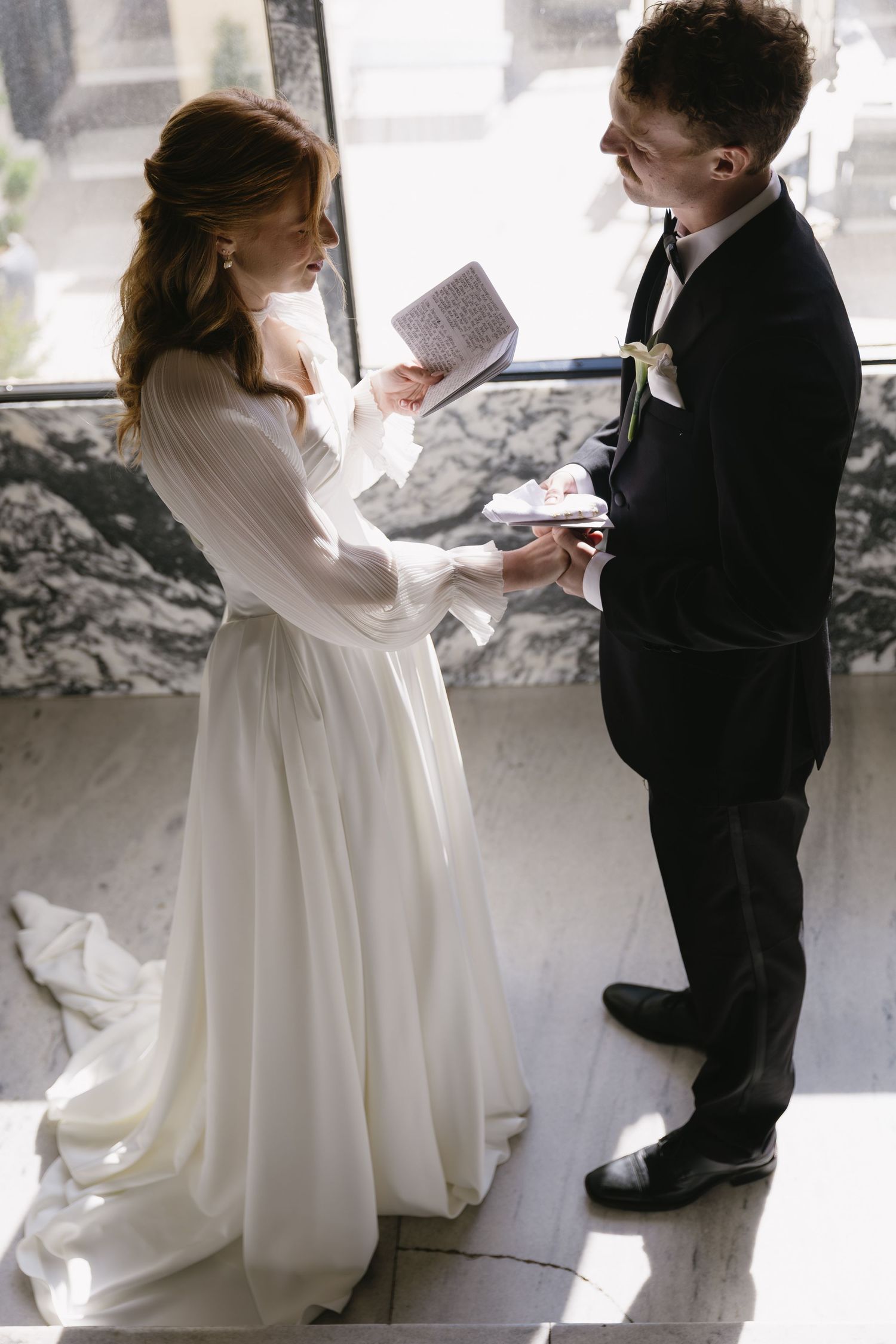 A tender moment captured between a bride in white and young ring bearer in black suit by a sunlit window.