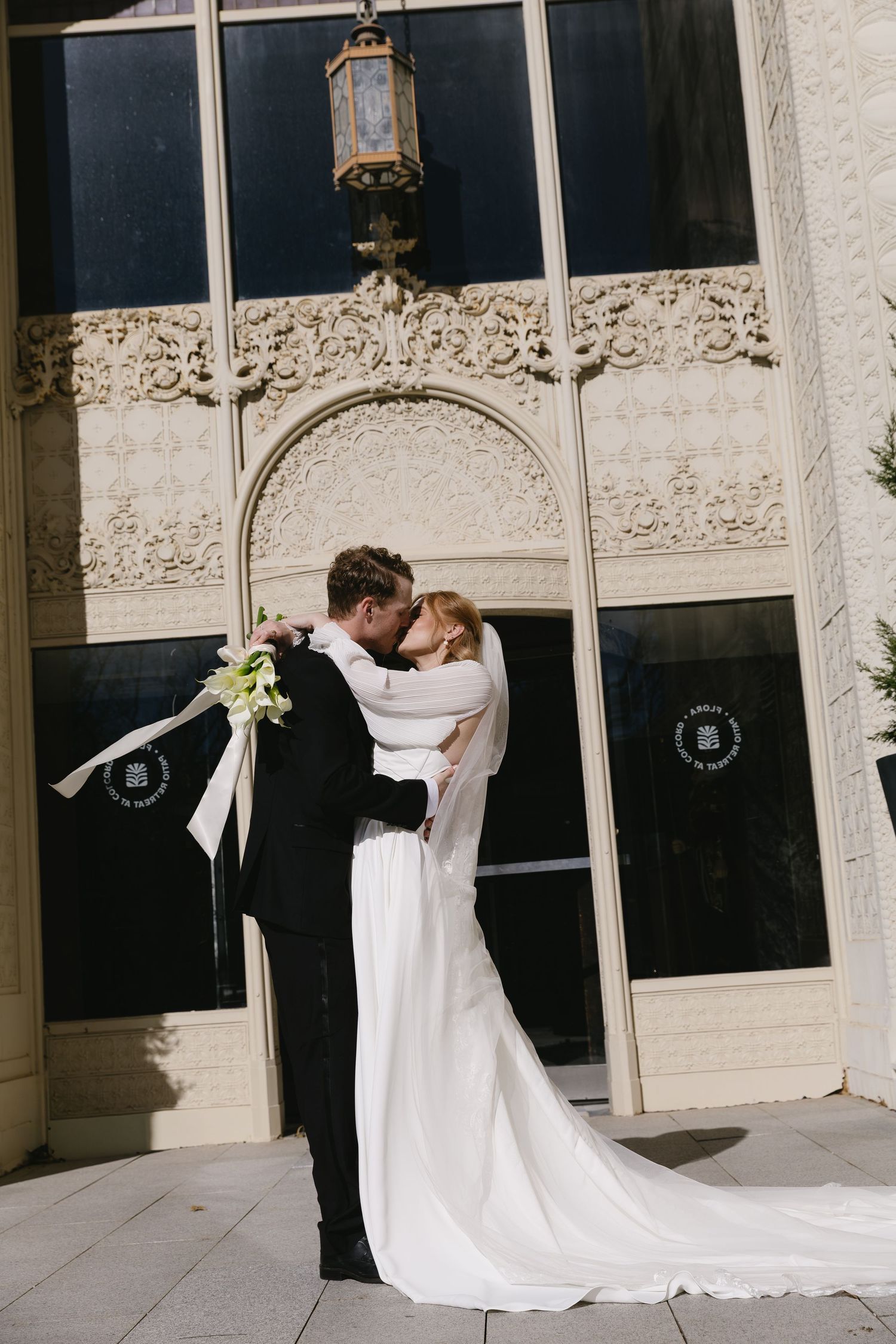 Bride and groom share intimate moment outside ornate architectural building.