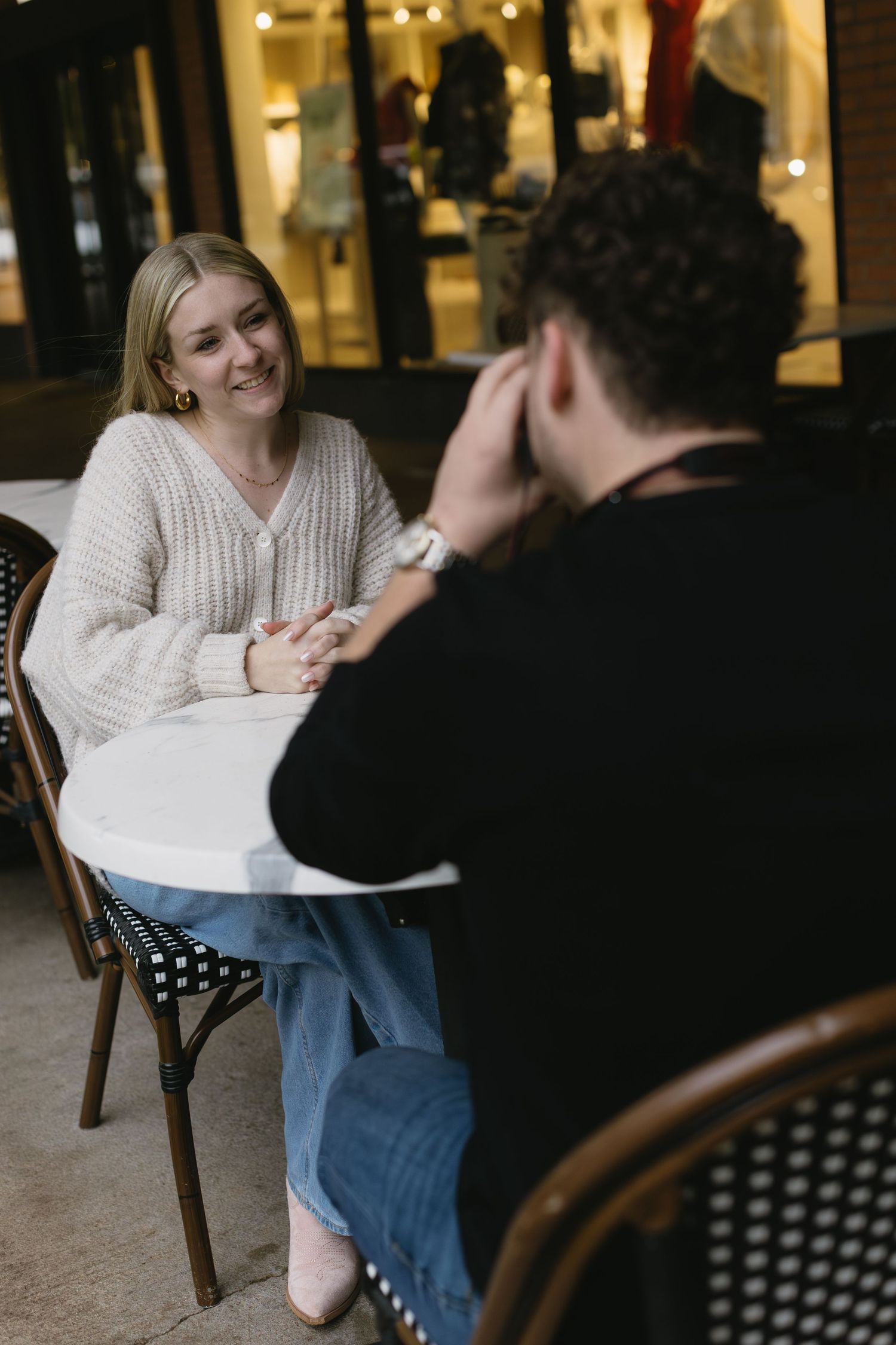 A couple shares a romantic moment at an outdoor cafe with twinkling lights in the background.