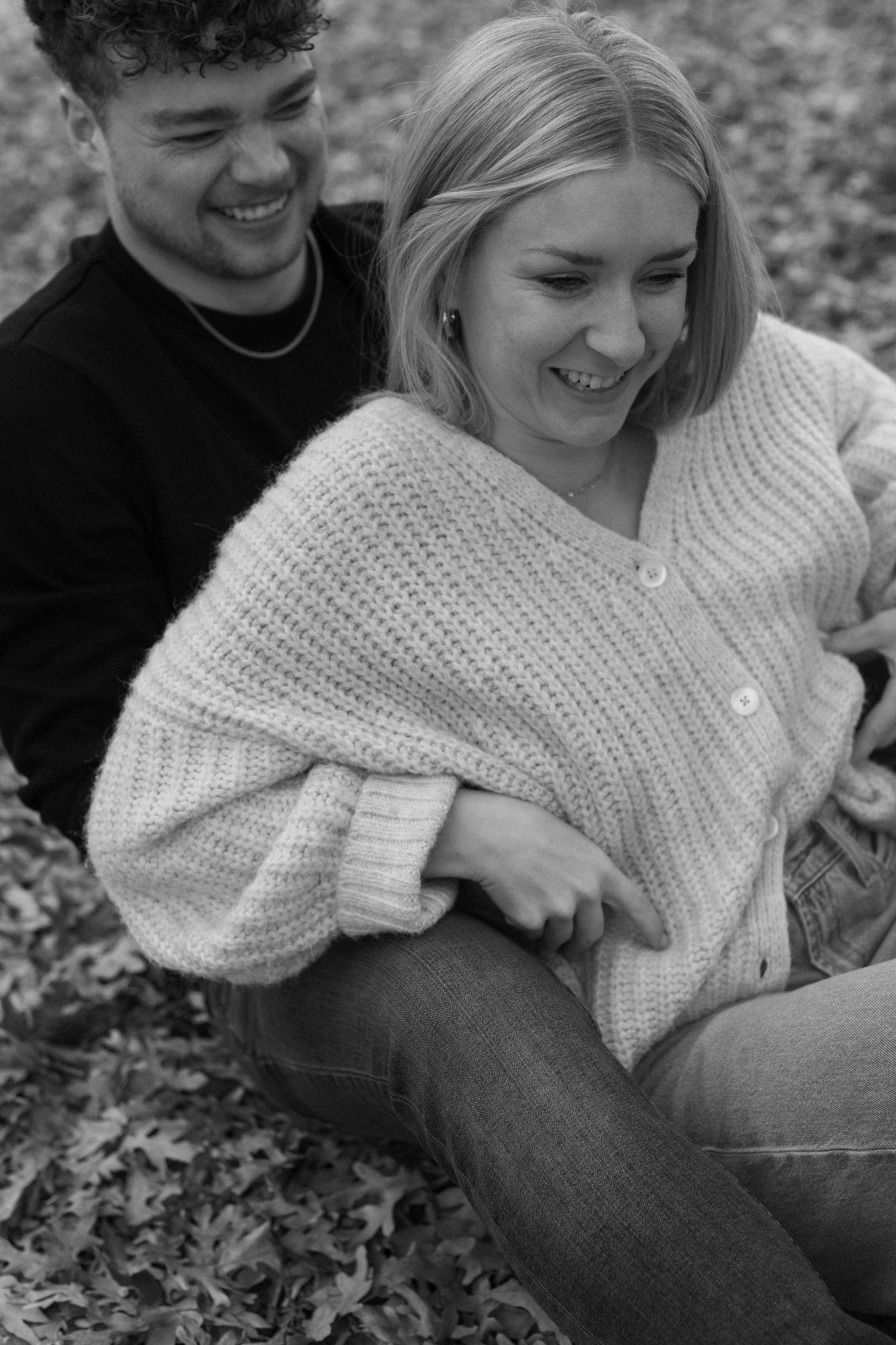 A black and white photo captures a couple sharing a joyful moment outdoors.