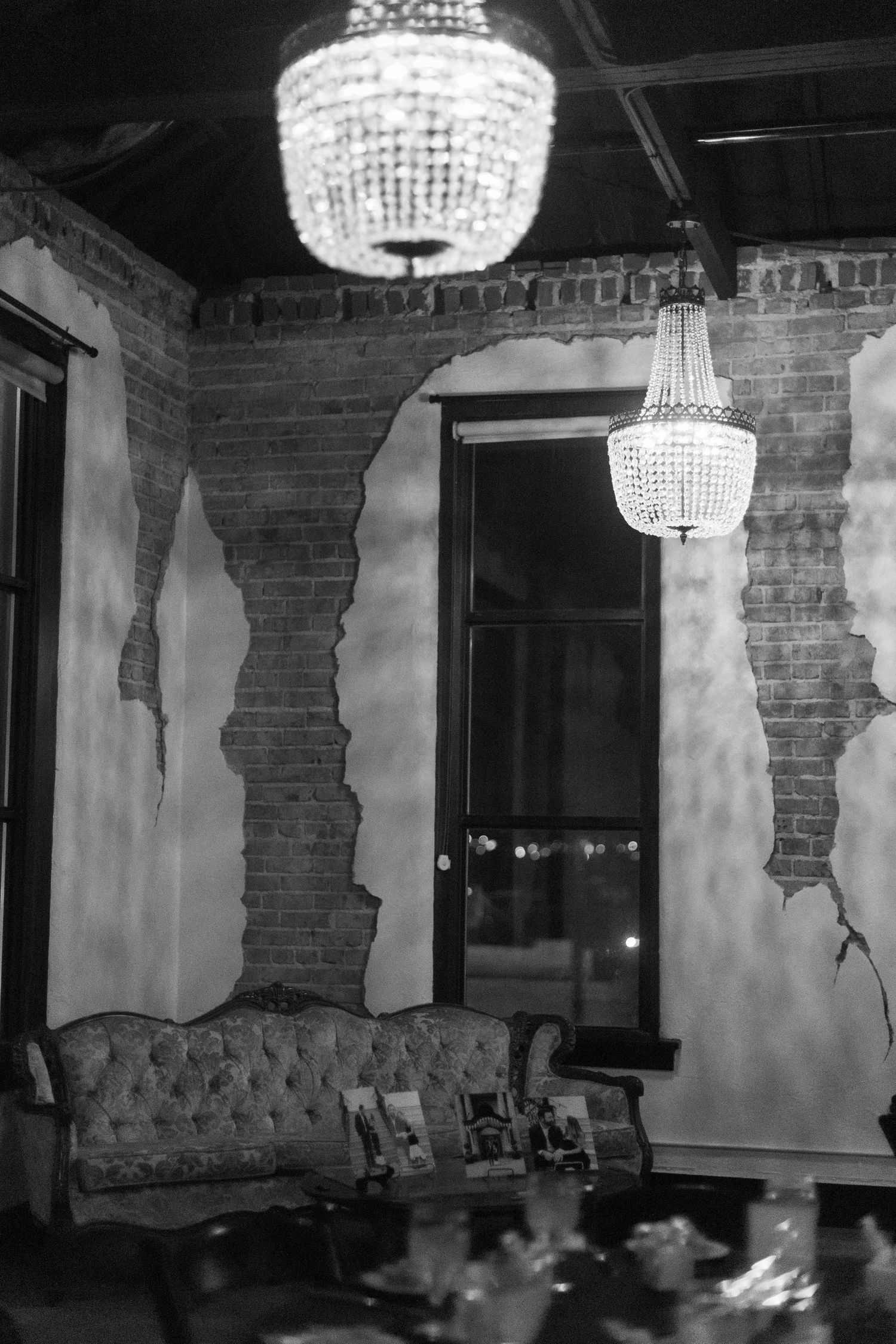 Crystal chandeliers illuminate an elegant room with exposed brick walls and vintage furniture.