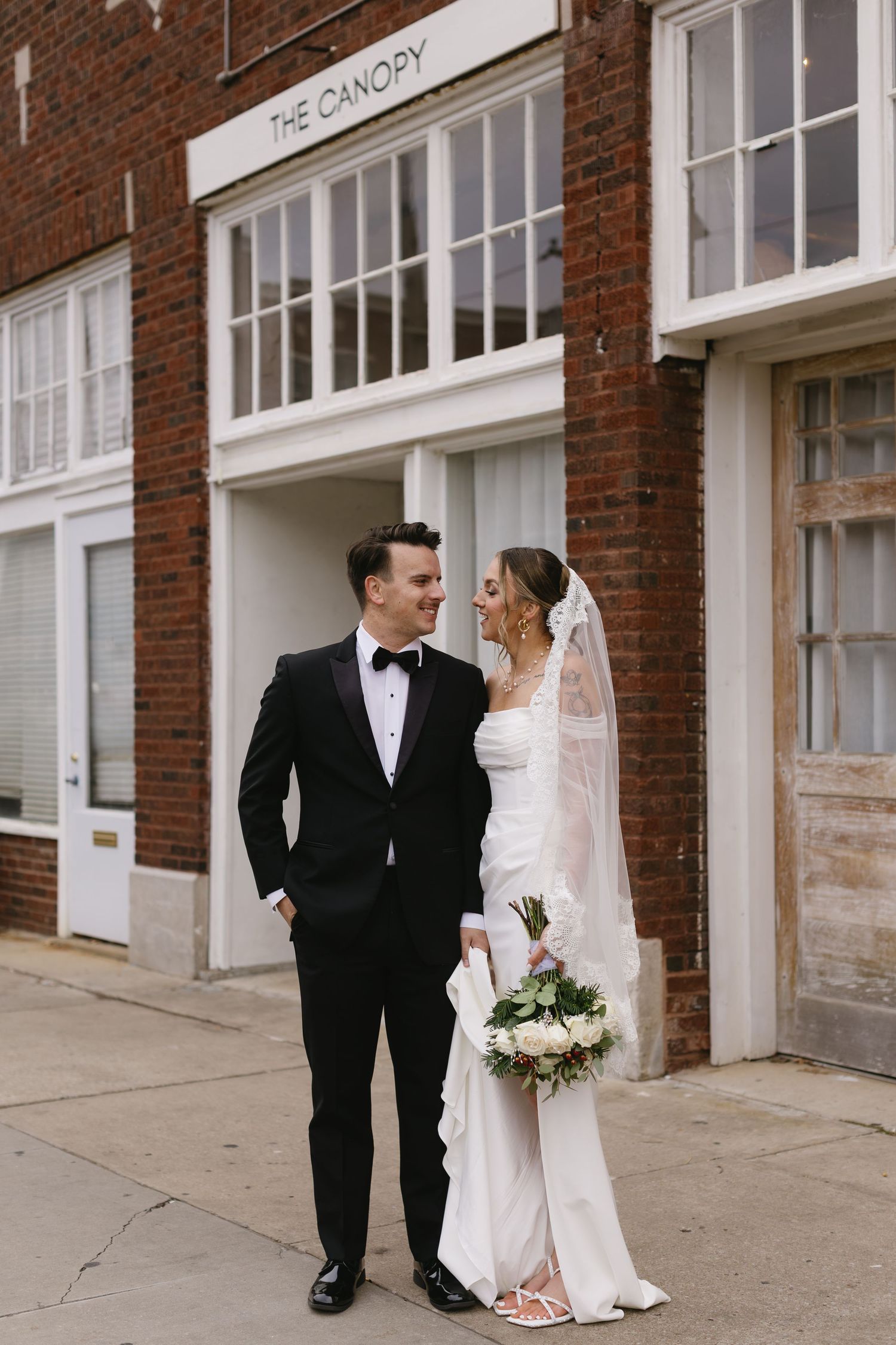 Wedding couple poses together against brick building exterior in classic formal attire.