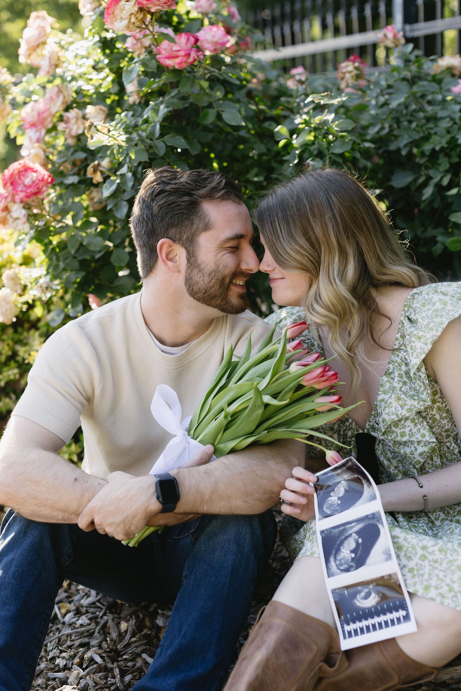 A sweet spring pregnancy announcement moment in a garden with pink roses, tulips and an ultrasound photo.