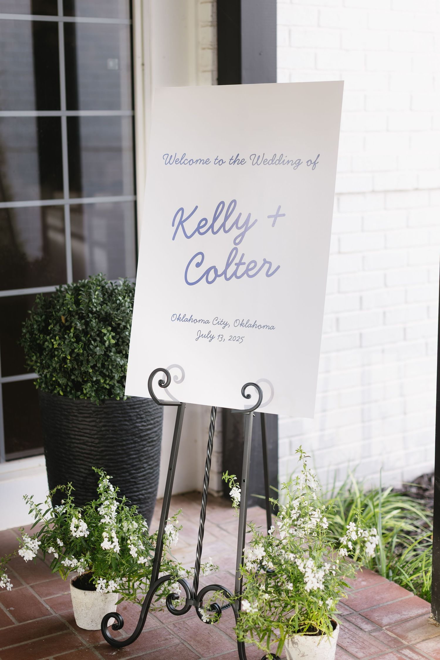 Wedding signs with elegant calligraphy displayed on decorative stands next to white floral arrangements.