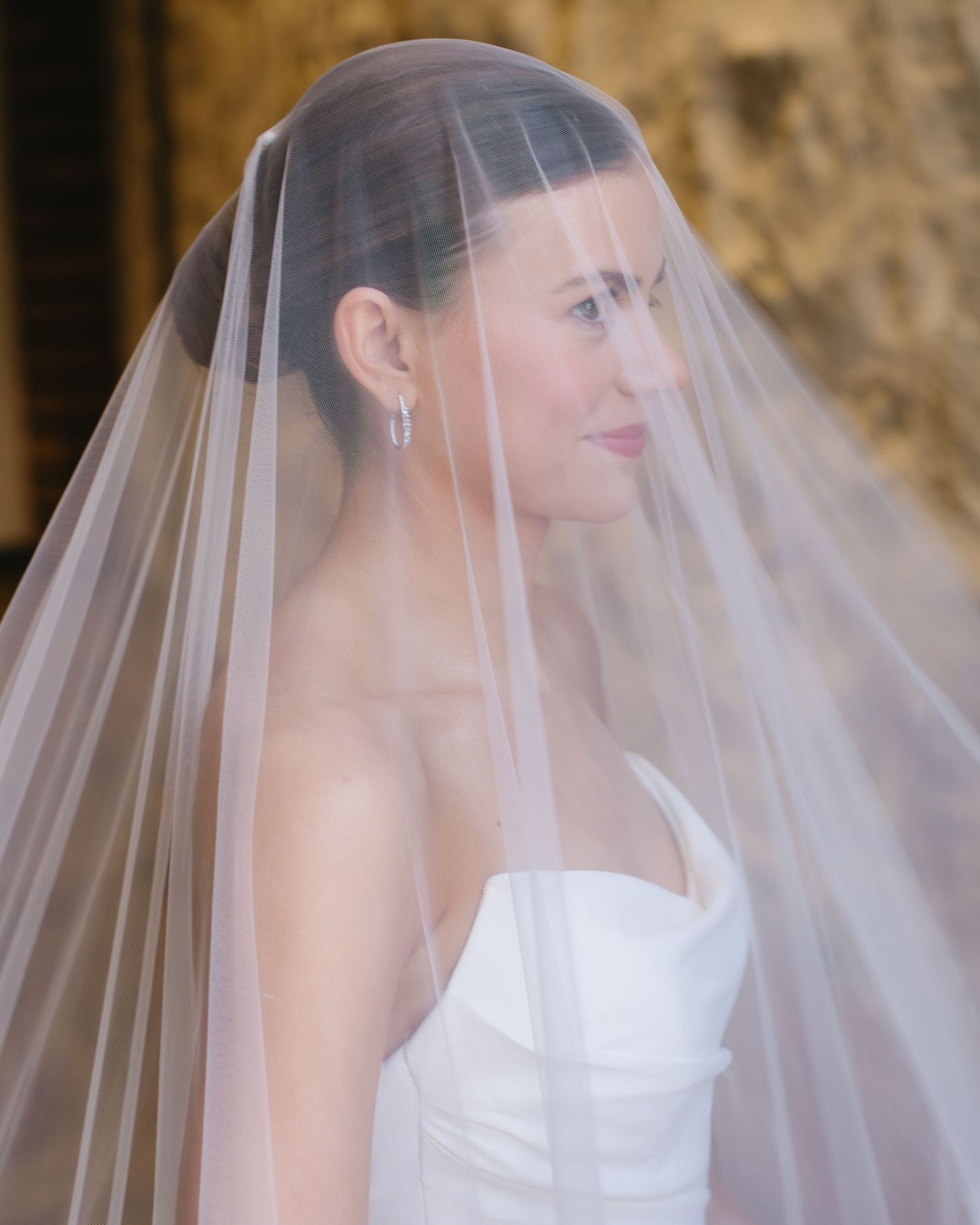 Elegant bride wearing white wedding gown with flowing sheer veil in romantic side profile.