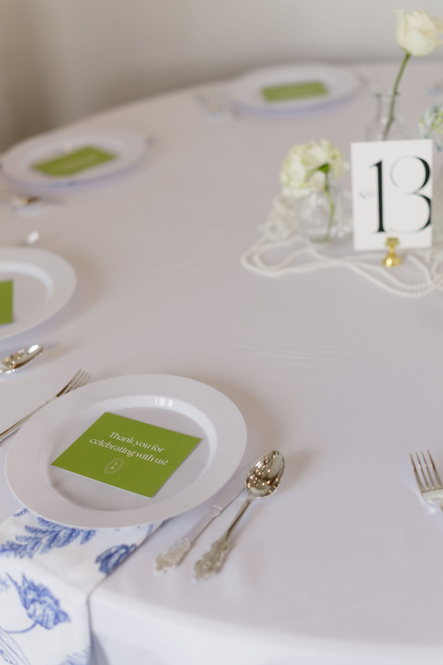 Minimalist wedding table setting with white linens, blue accents, and table number card.