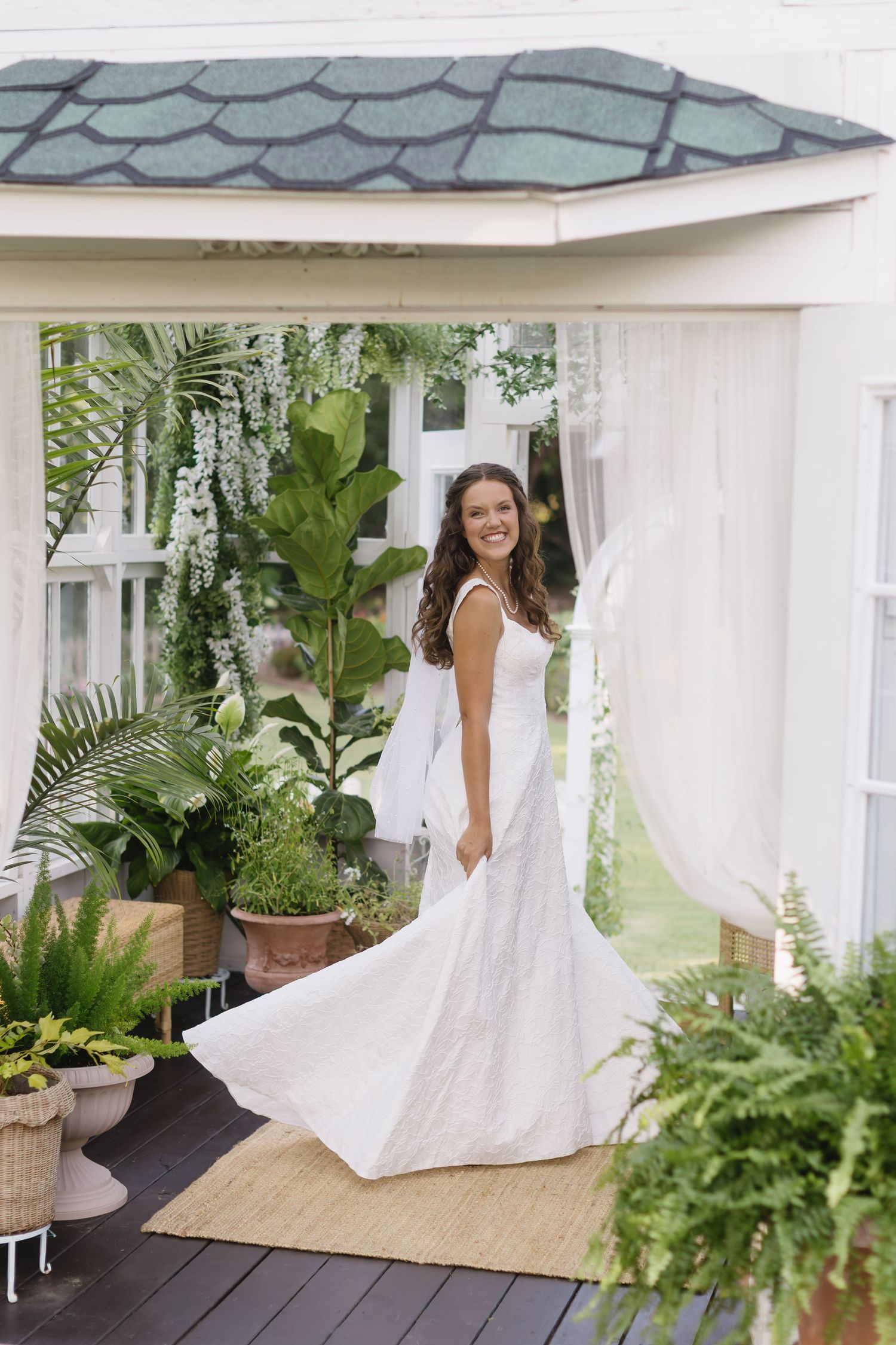 A flowing white wedding dress twirls on a covered patio surrounded by lush tropical plants and white curtains.