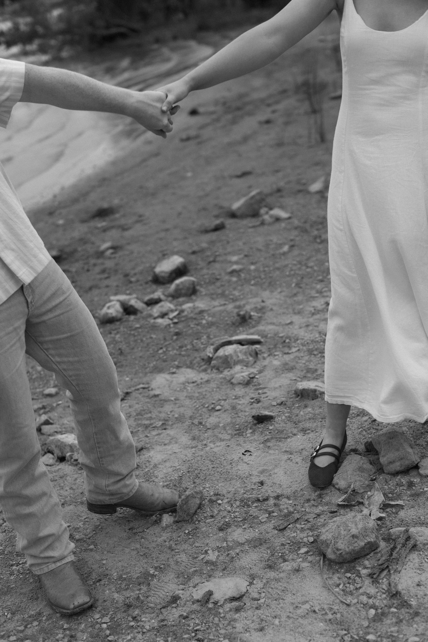 Black and white lower body shot of couple walking on rocky shoreline.