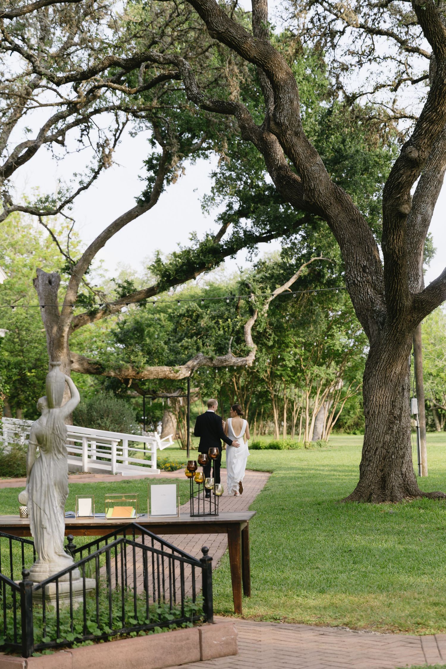 Tranquil outdoor wedding venue with white statues decorating a pathway through lush green gardens.