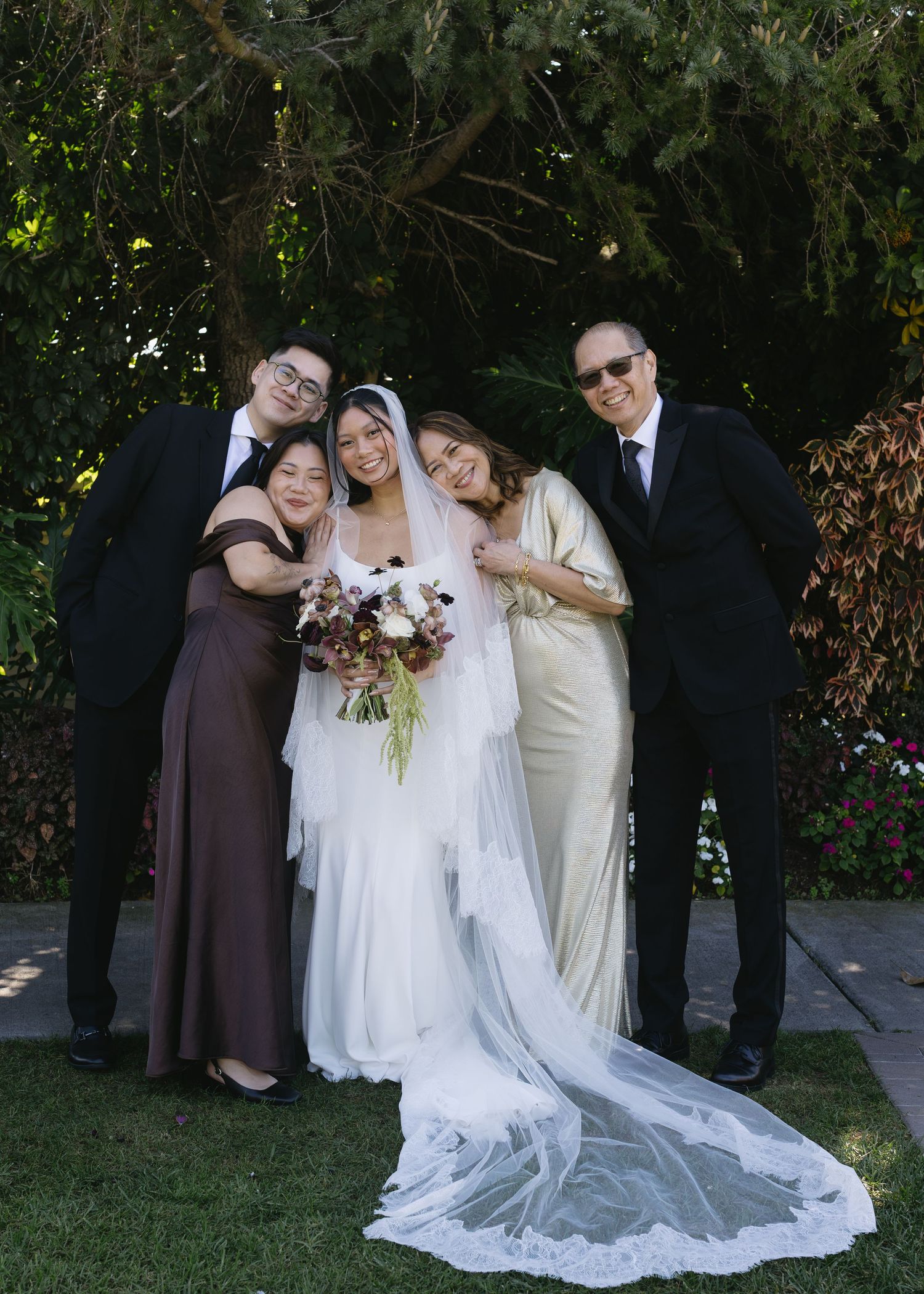 Wedding party poses together outdoors with bride in flowing white dress and attendants in brown and cream gowns.