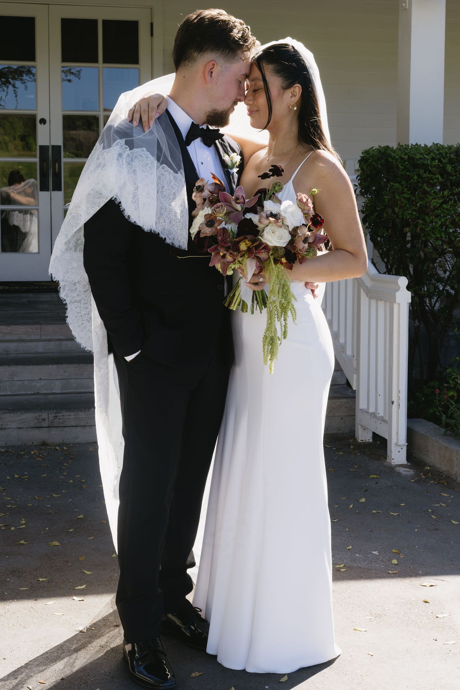 Newlyweds share a romantic moment under a white columned porch on their wedding day.