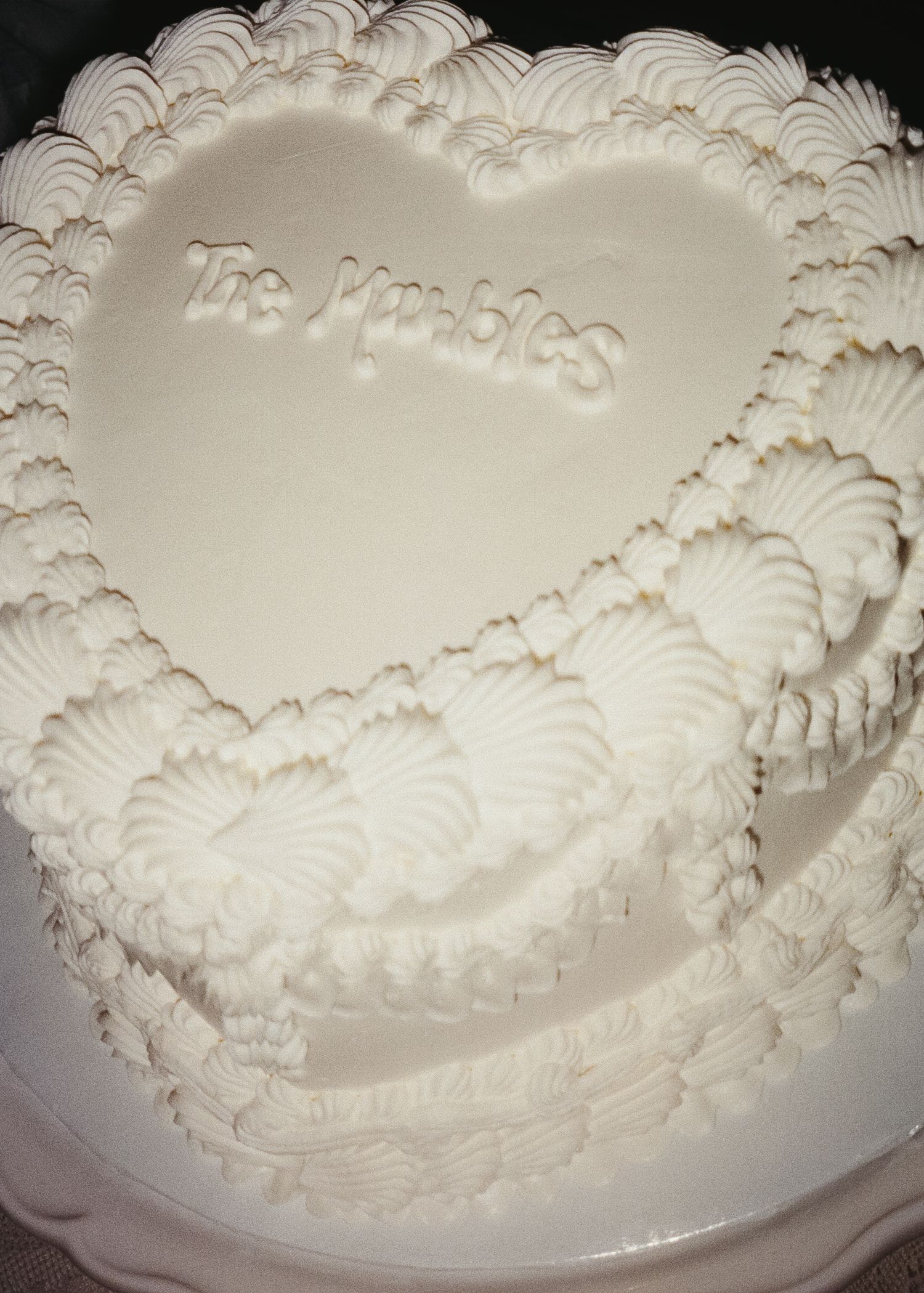 Ornate white wedding cake with intricate piped frosting details in a classic swirled pattern.