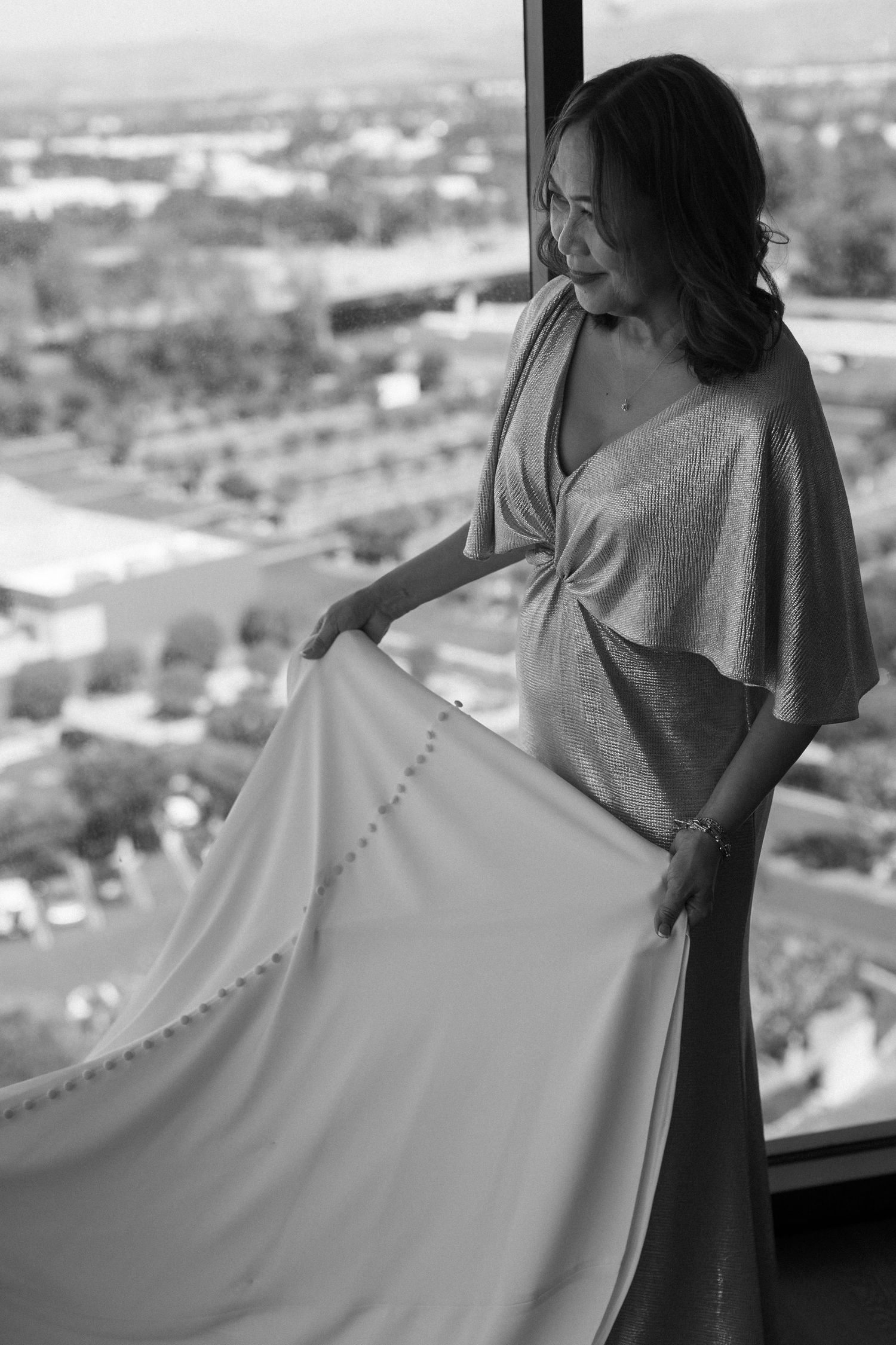 Silhouette of someone holding up a flowing white wedding dress against a cityscape view.