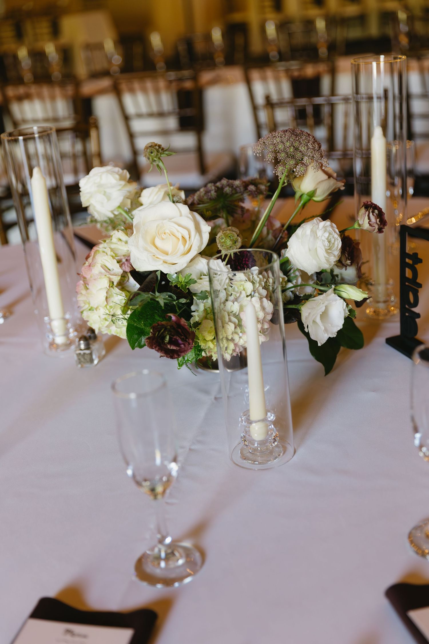 Elegant white rose centerpiece with glass candle holders on a wedding reception table.