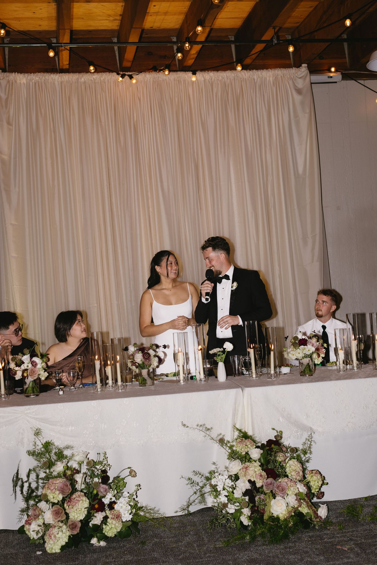 Wedding reception head table decorated with white floral arrangements and candlelight.
