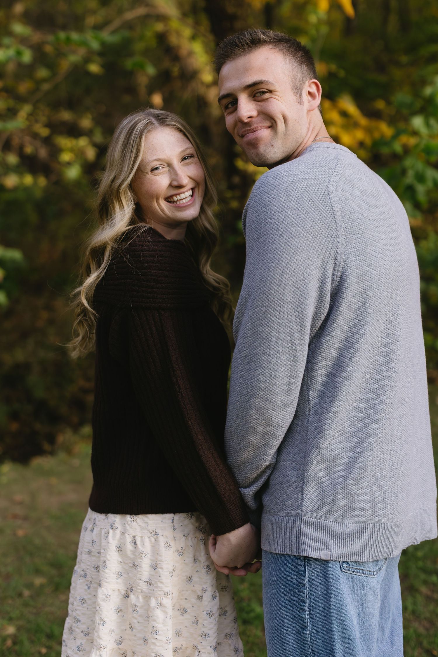 A romantic couple embraces while wearing casual clothing in a park during fall season.