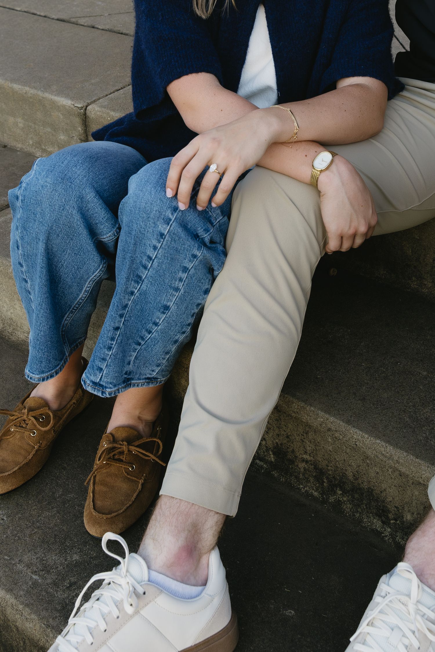 Detail shot of legs showing khaki pants and blue jeans with casual shoes sitting on concrete steps.