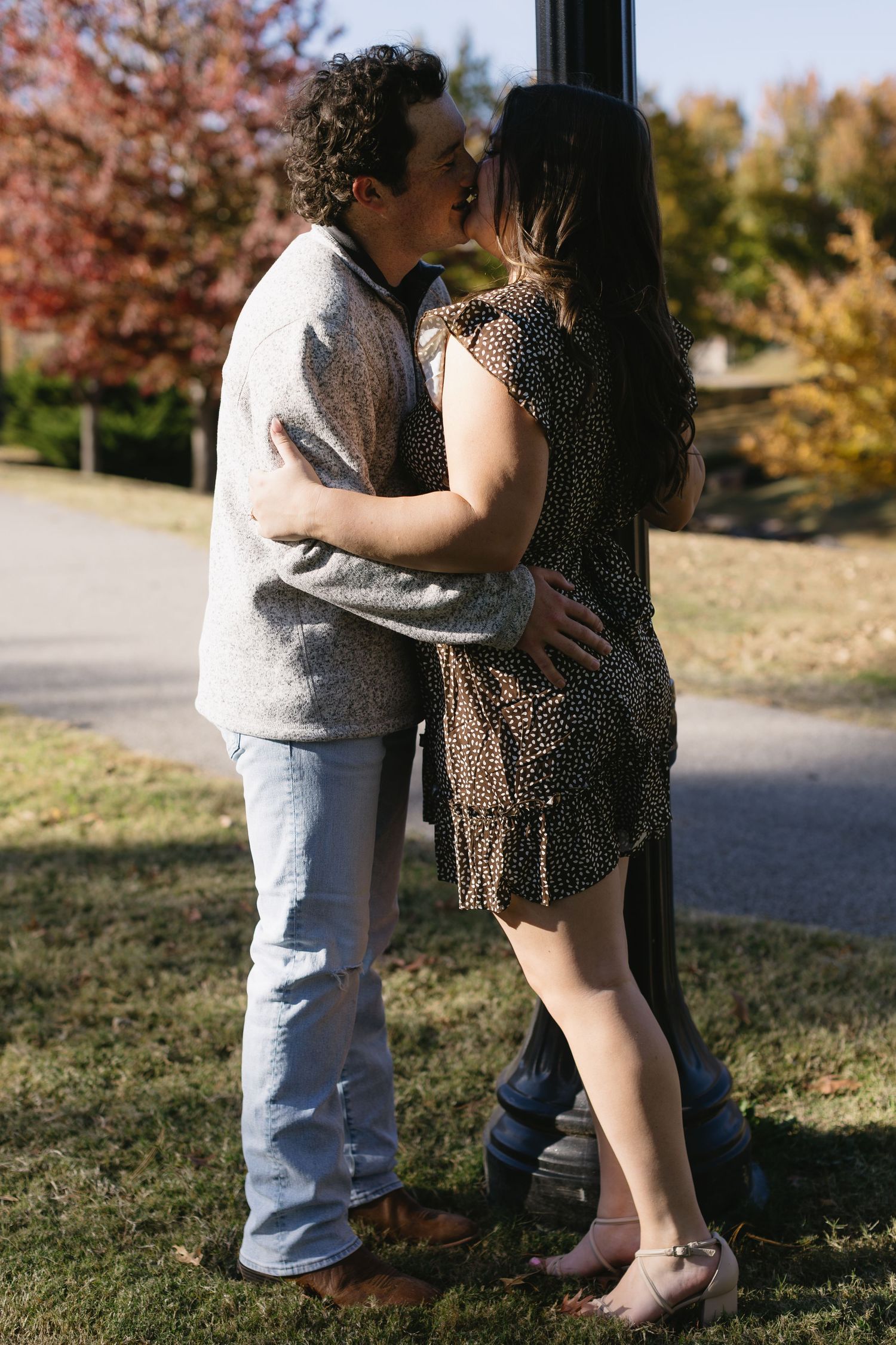 Couple shares an intimate moment while standing together on grass during fall season.