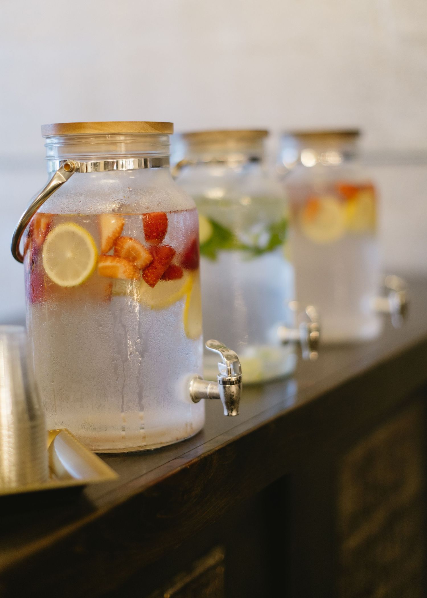 Row of glass dispensers filled with colorful fruit-infused water on a dark counter.