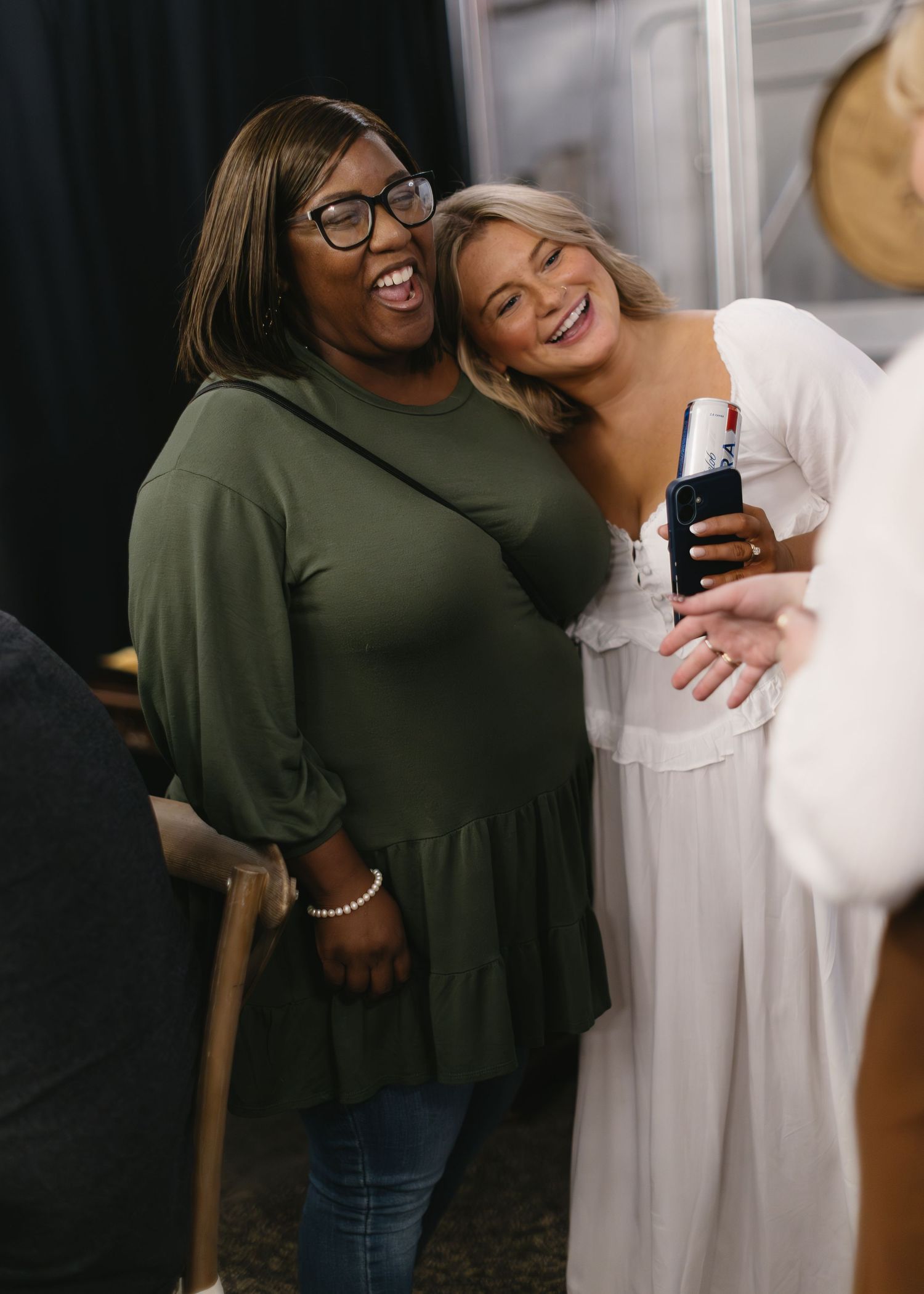 Friends sharing joyful laughter and embraces in a casual indoor setting.