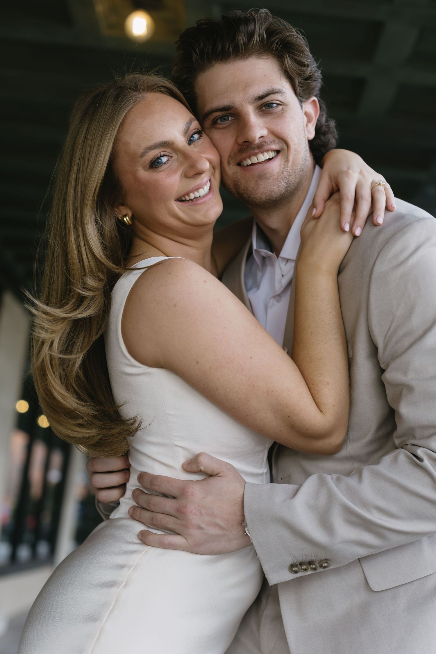 A romantic couple shares an intimate moment in formal attire against a dark background with soft lighting.
