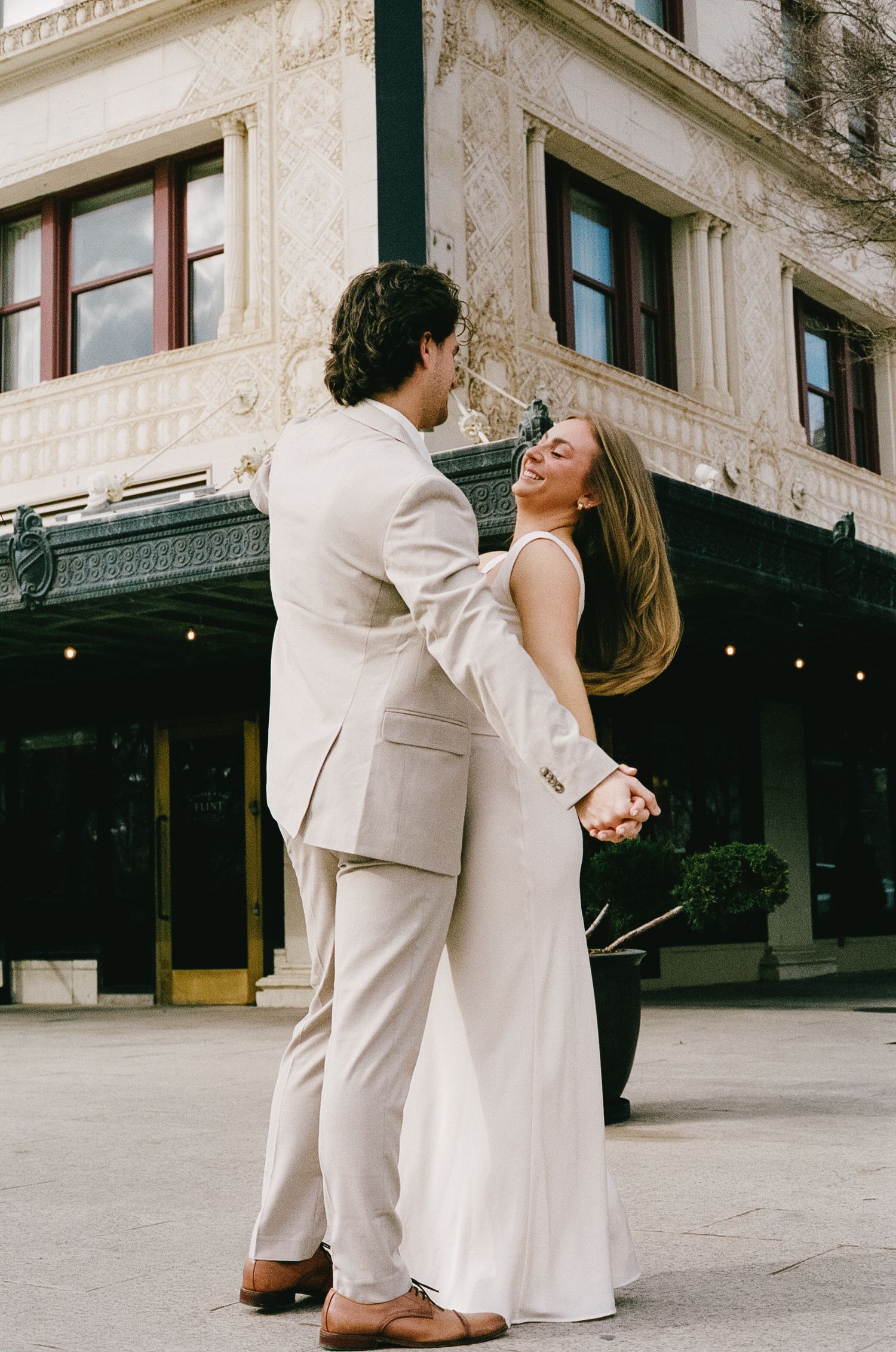 A couple in light formal wear shares a romantic dance moment outside a historic building.