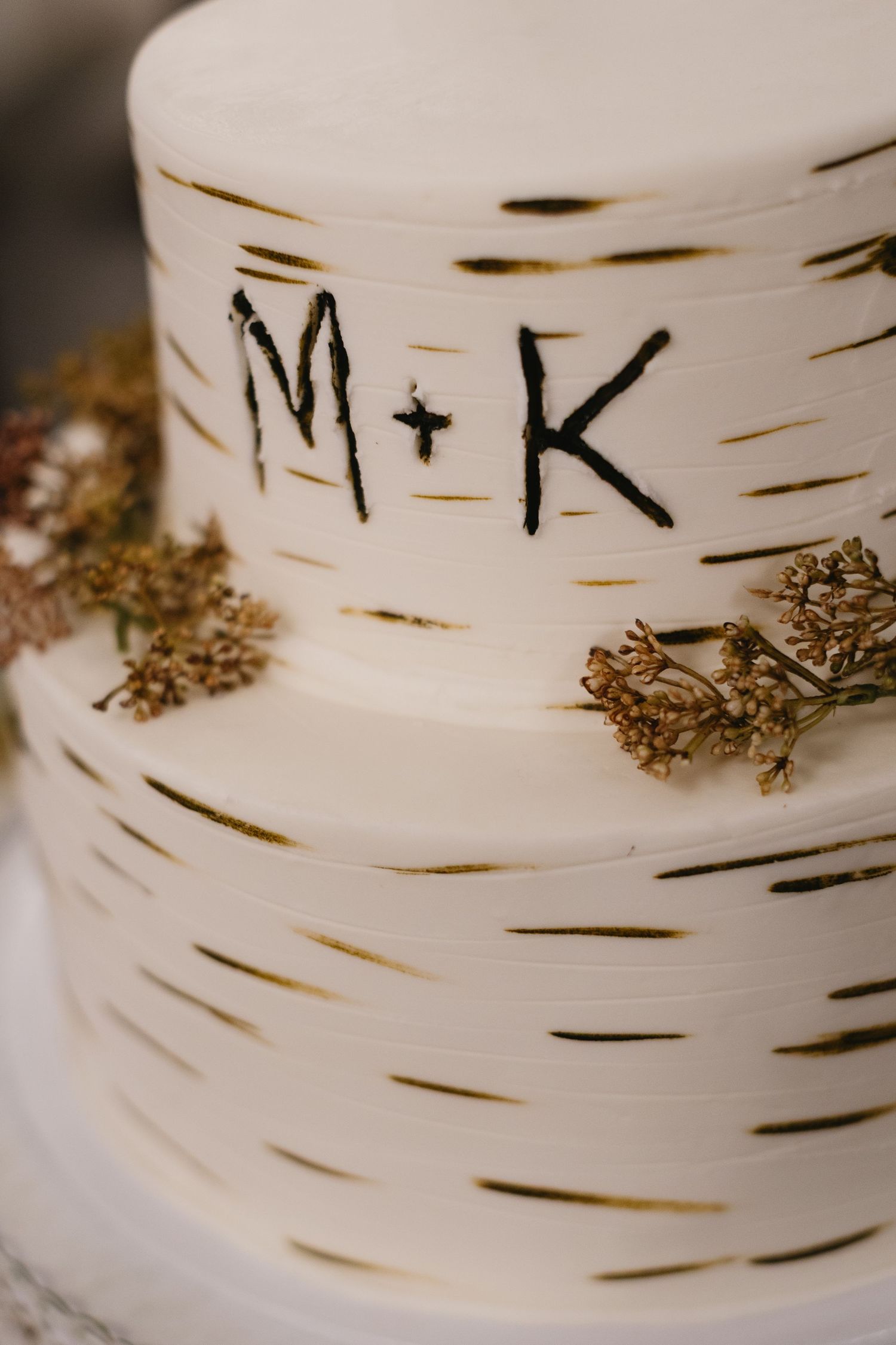 Close-up detail of a white wedding cake decorated with birch bark pattern and initials.