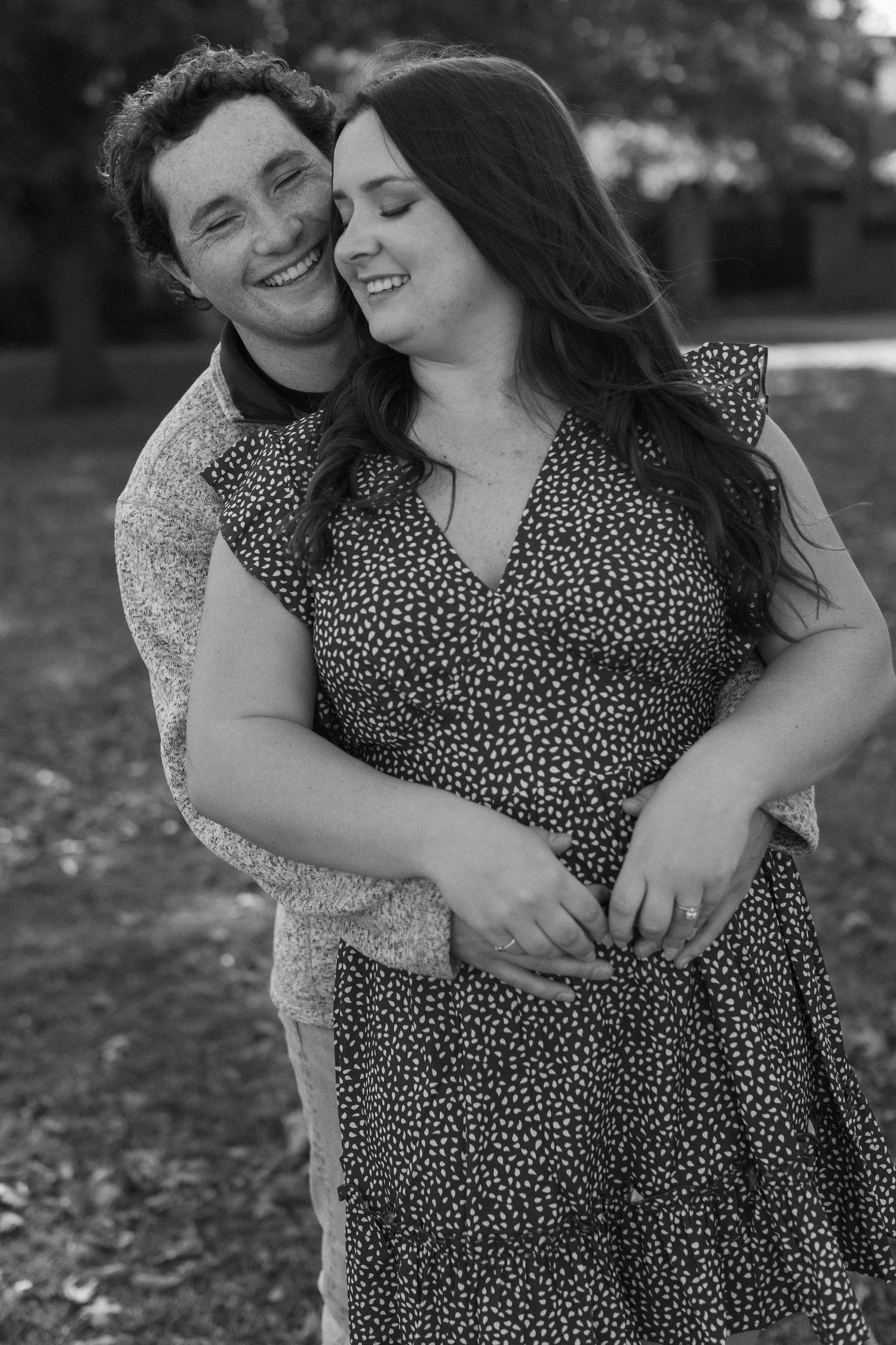 A couple embraces and laughs together during an outdoor black and white photoshoot.