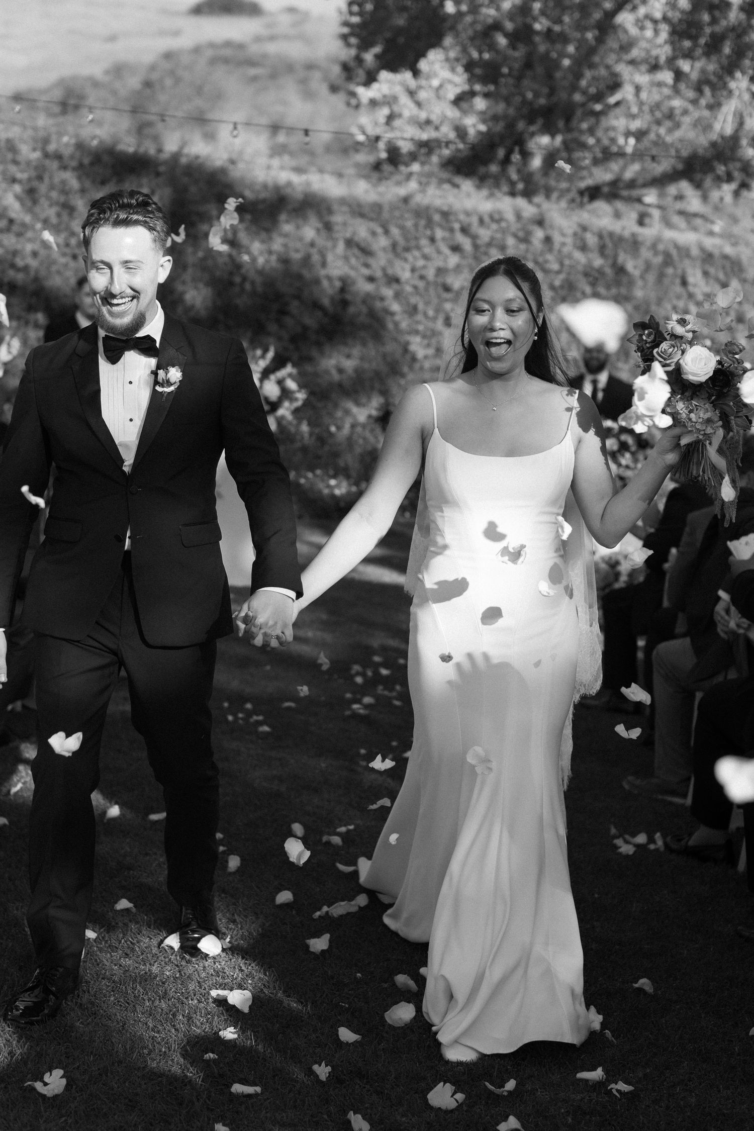 Wedding couple celebrates with flower petals being tossed in outdoor ceremony.