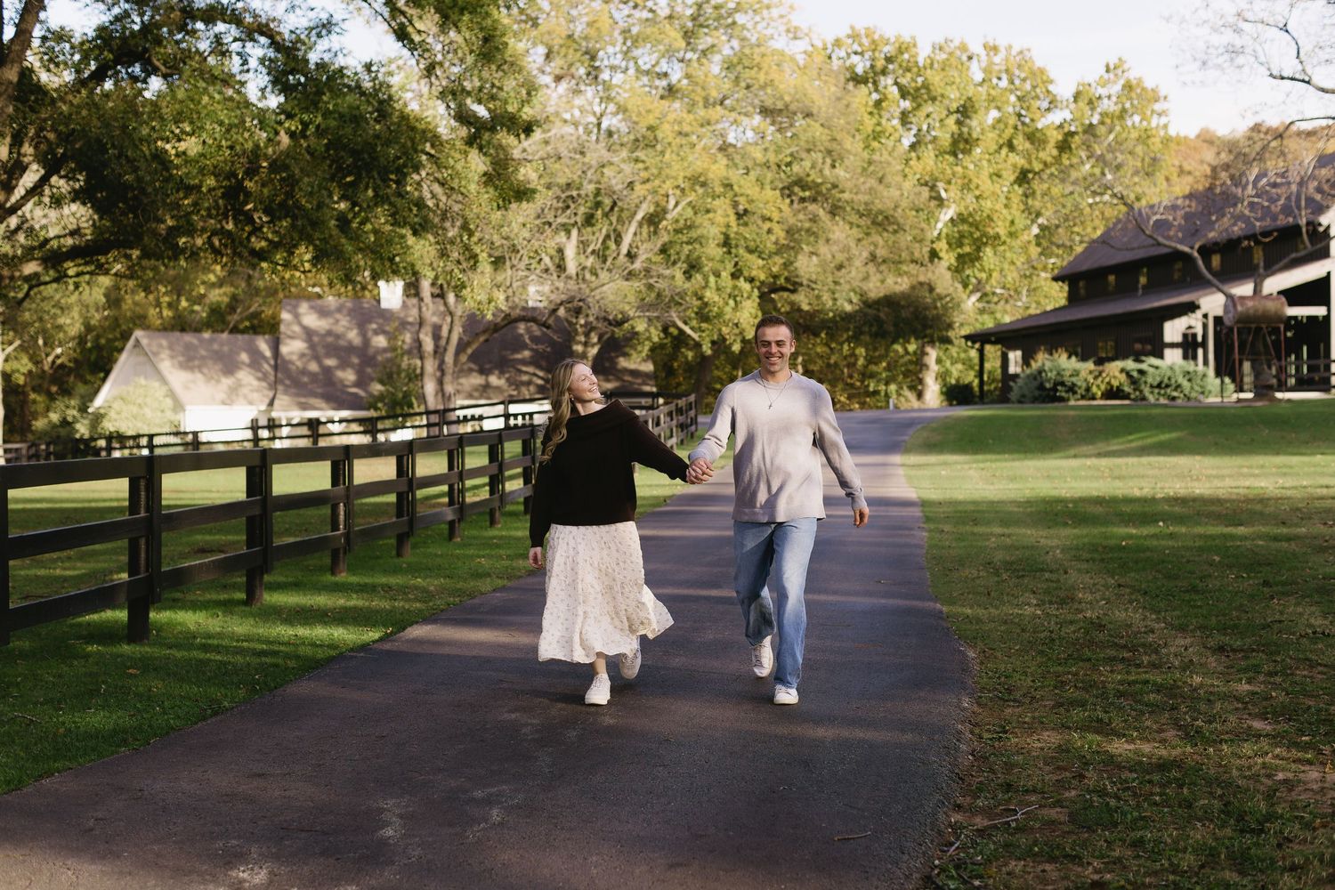 Wide landscape shot of a couple walking down a tree-lined path in a park.