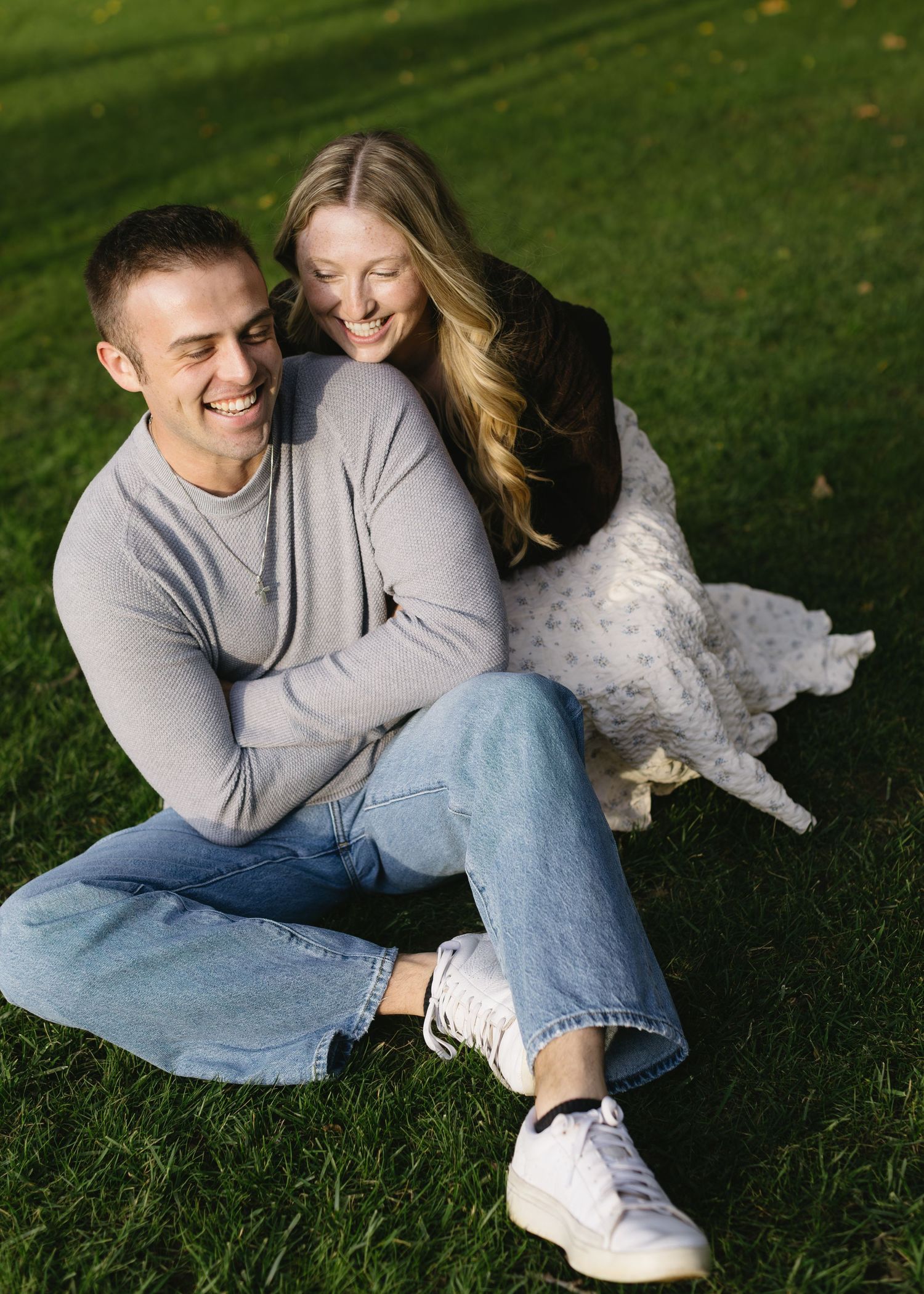 A couple shares a candid laughing moment while sitting together on grass.
