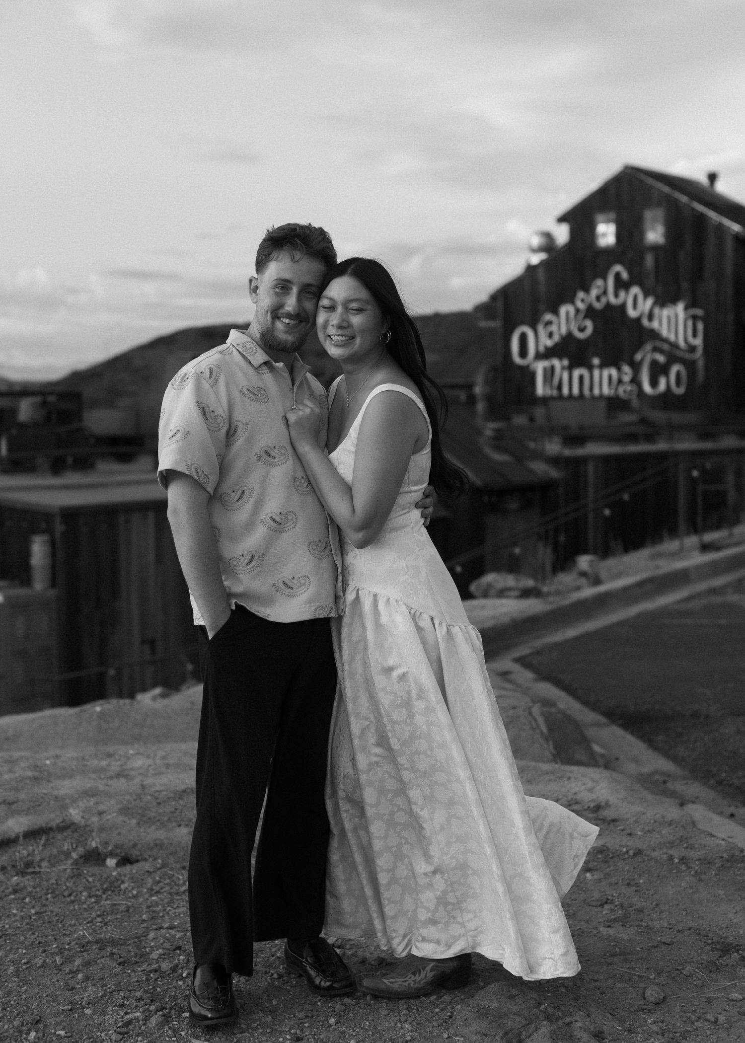 Black and white photo of a couple laughing together near vintage buildings.