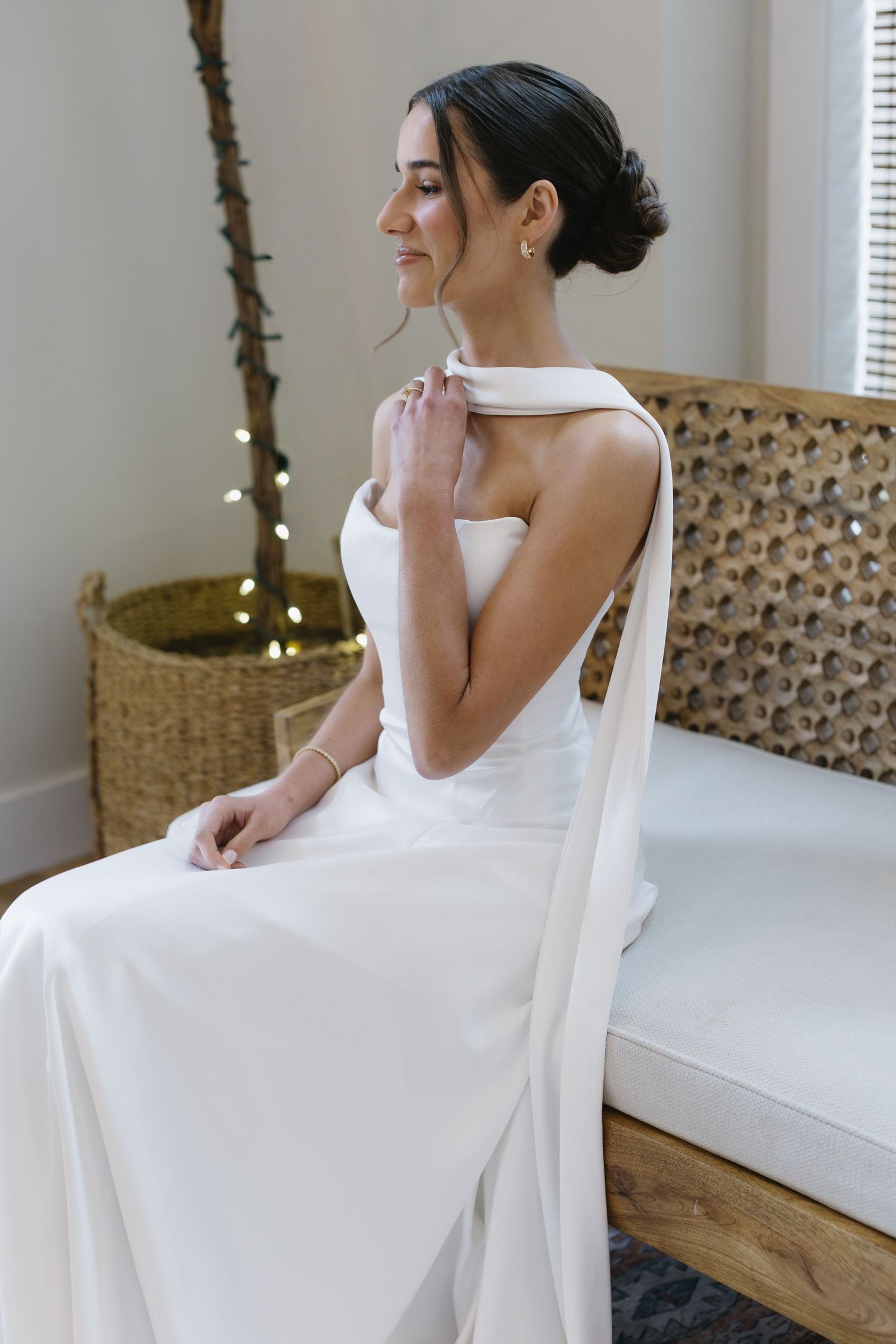 Elegant white wedding dress photographed in a minimalist interior setting with natural lighting.