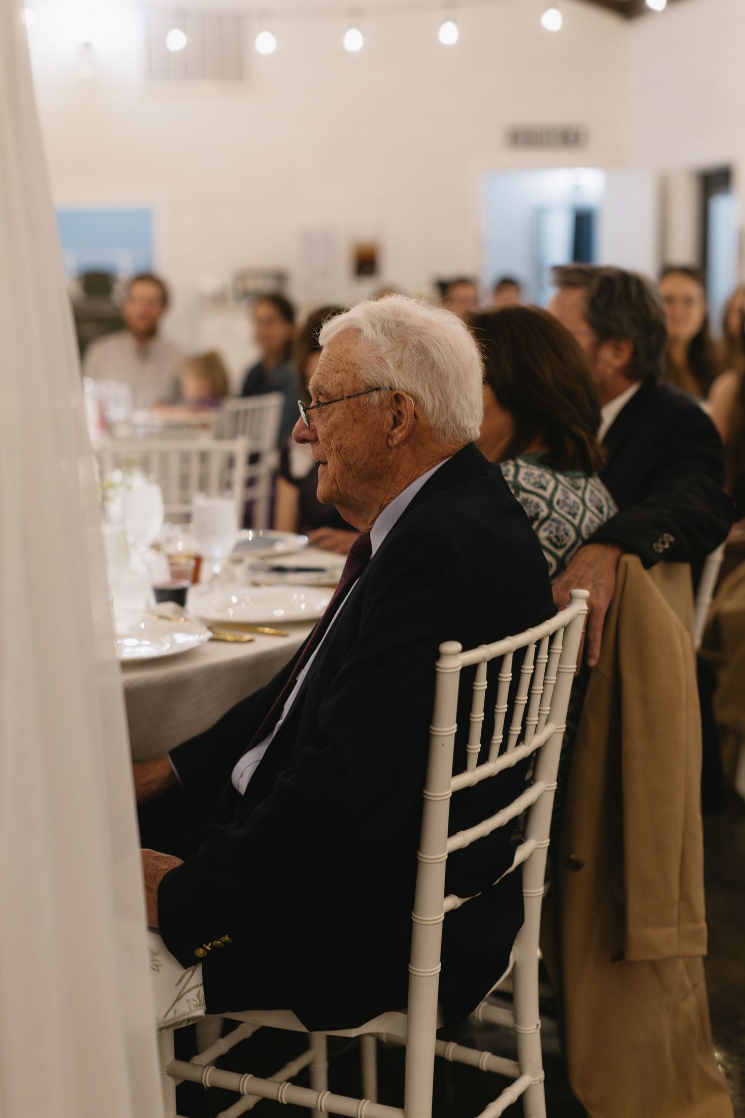 Wedding guests seated at white dining tables during an indoor reception.