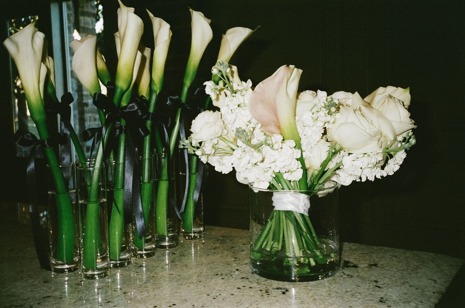 Elegant white floral arrangements with green stems displayed in glass vases at a wedding reception.