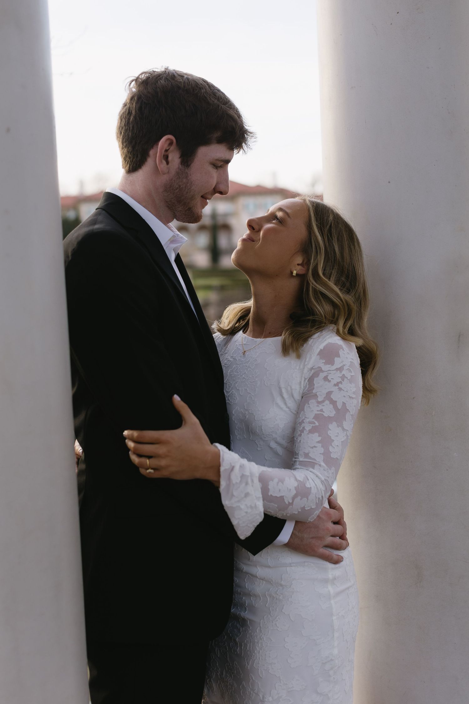 A tender moment between a couple framed by white columns during their wedding shoot.