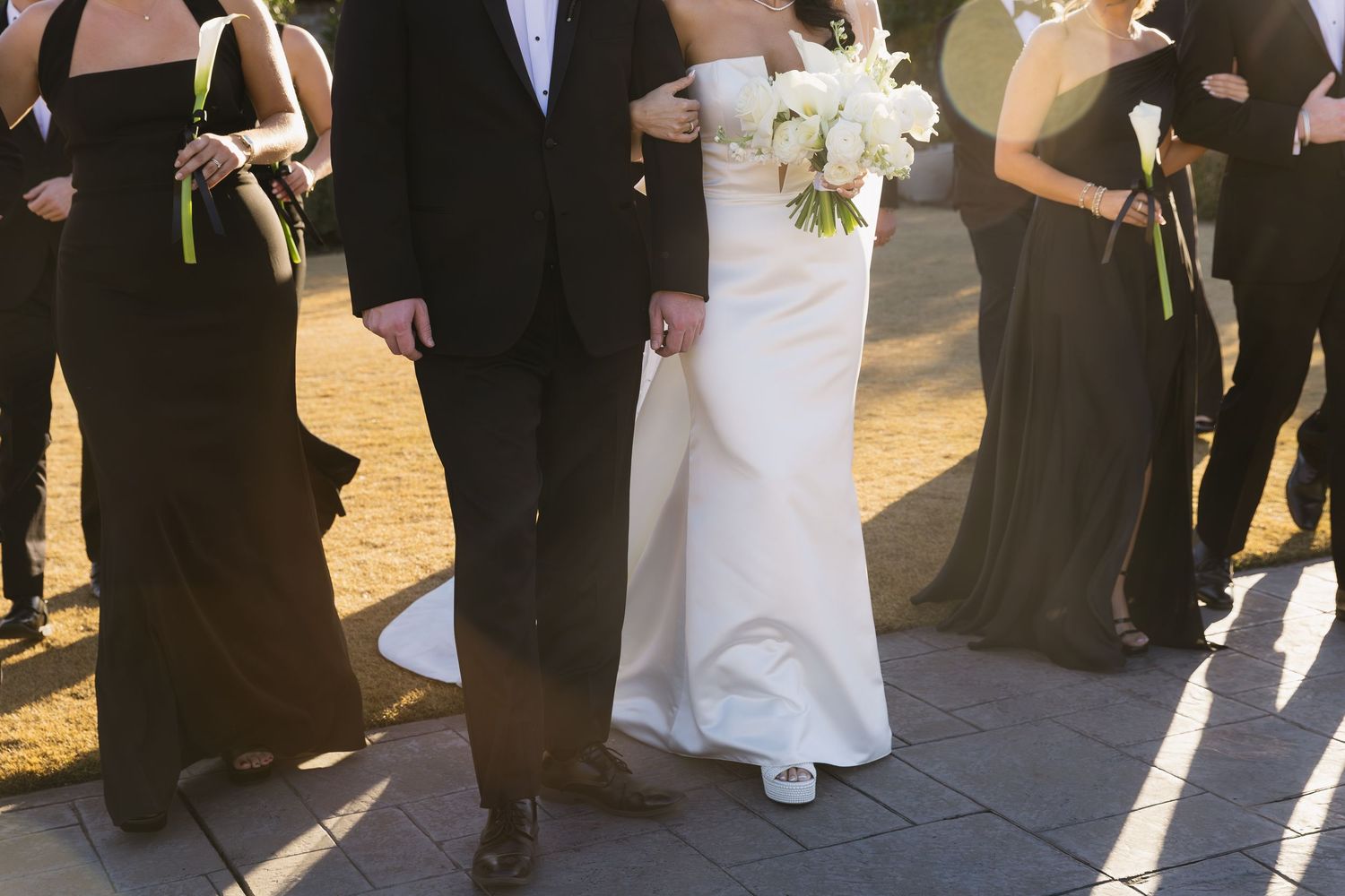 Wedding party members in formal black attire gather outdoors for photos.