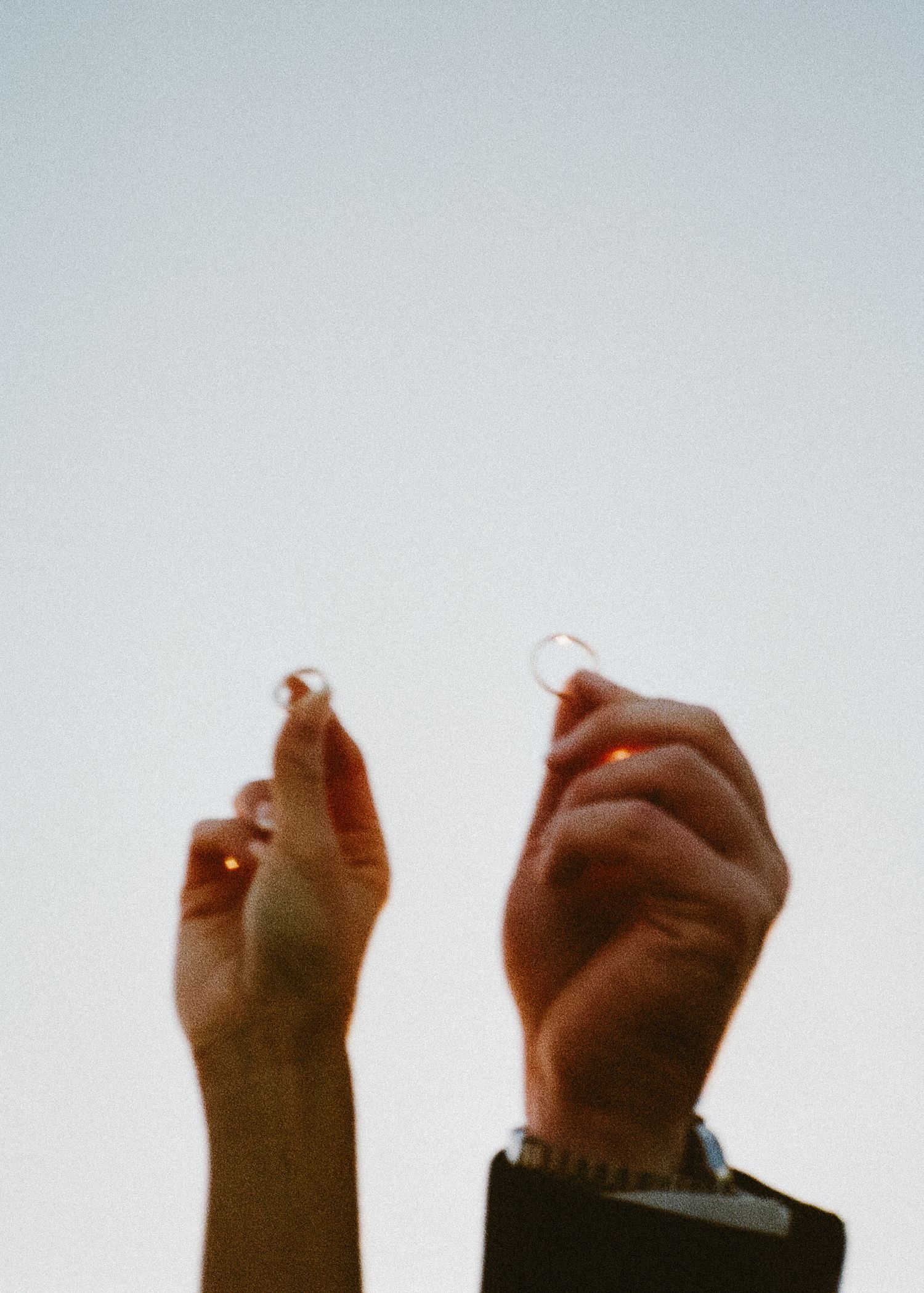 Two hands raised against light sky holding small objects.