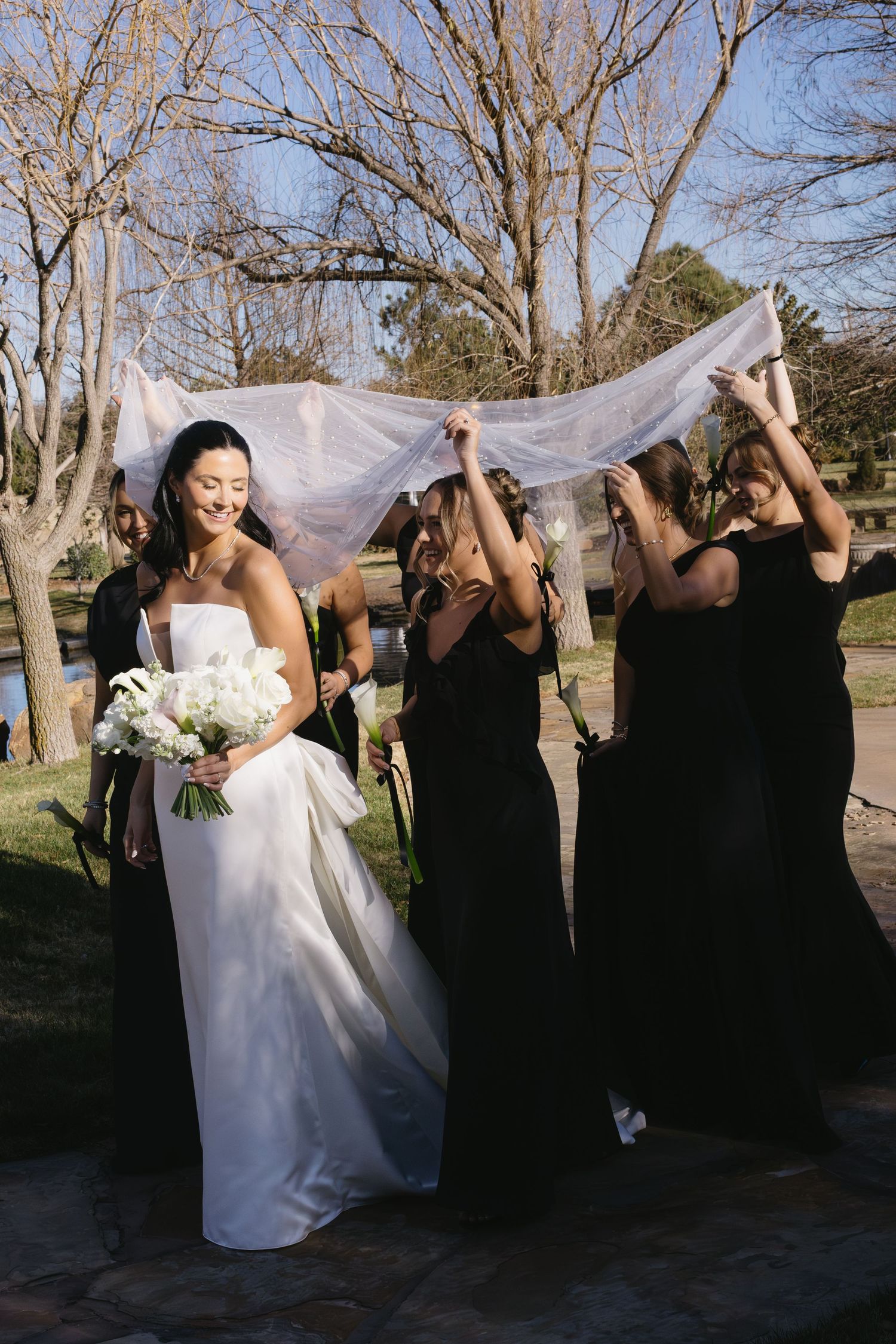 Wedding party in black dresses holding up the bride's veil in a playful outdoor photo sequence.