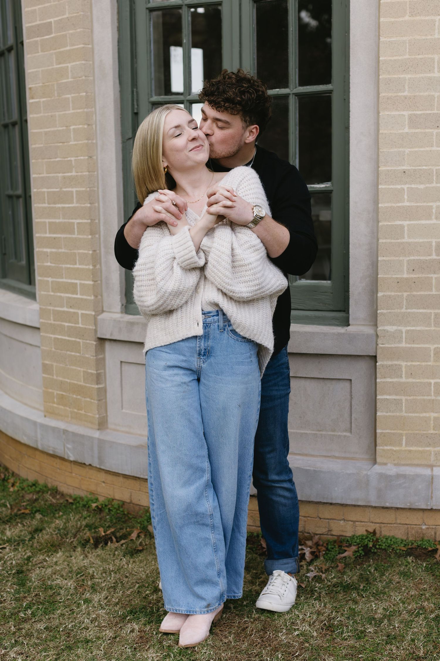 Candid moments of a couple embracing outside a brick building with windows.