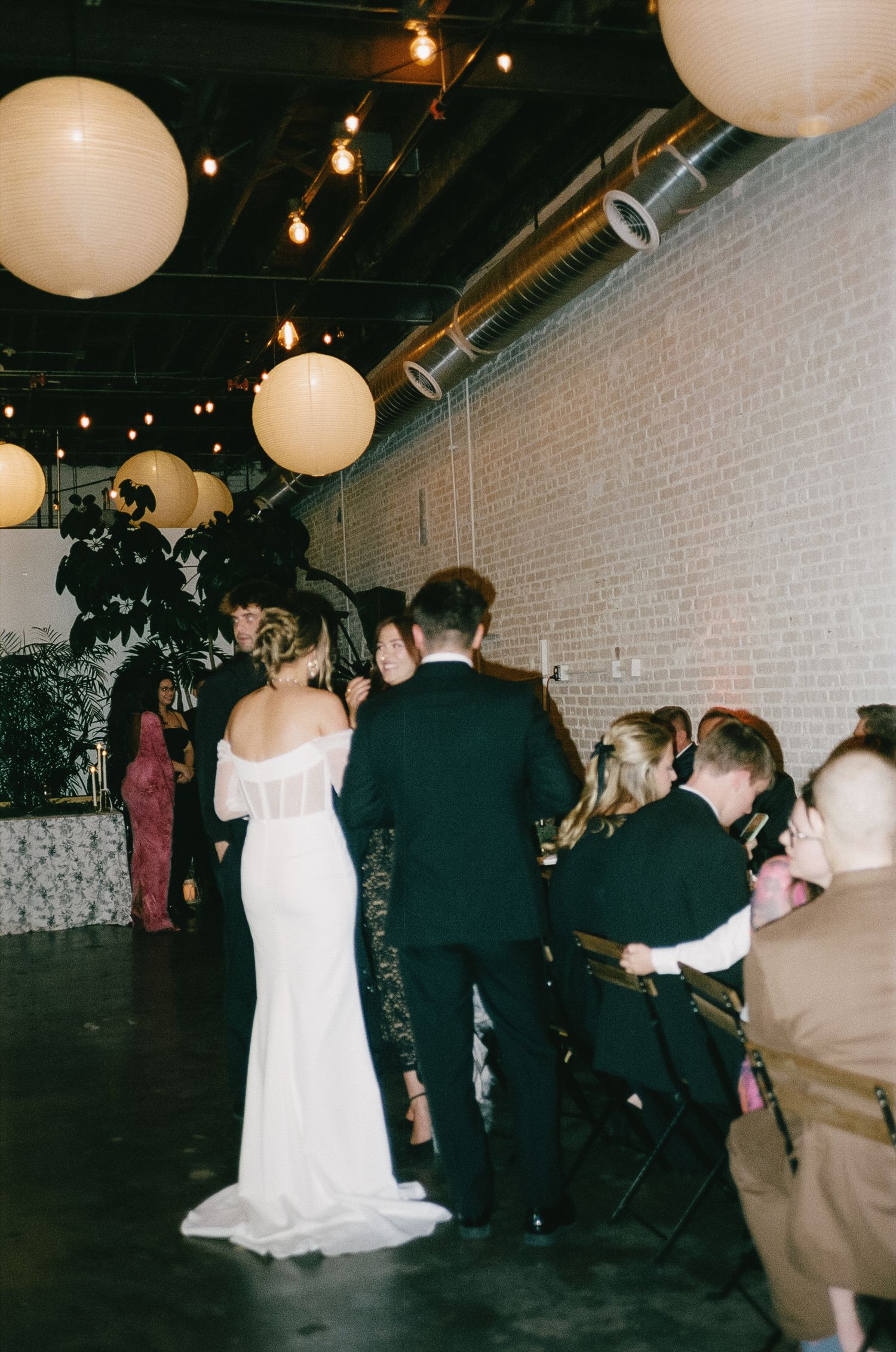 Wedding reception in industrial venue with white lanterns and string lights.