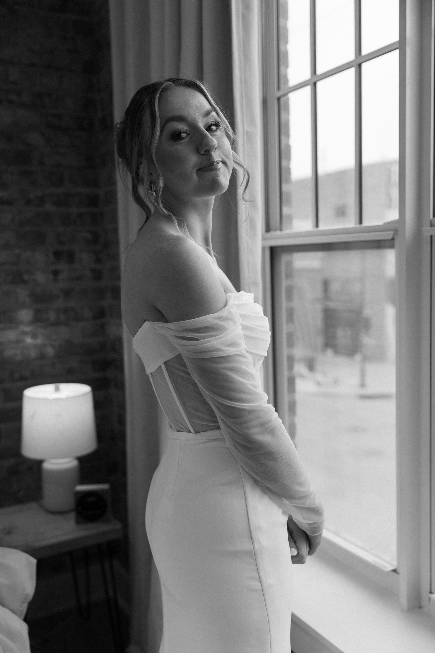 Elegant white wedding dress with sheer sleeves photographed near a bright window.