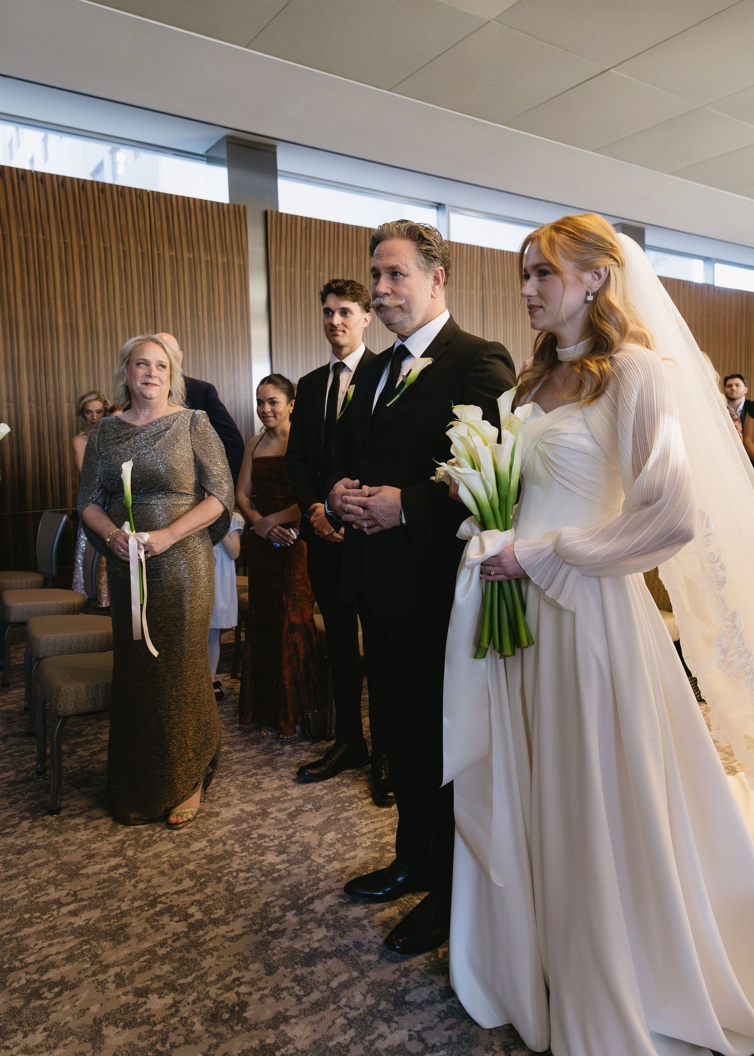 Wedding ceremony procession in a carpeted room with guests watching.