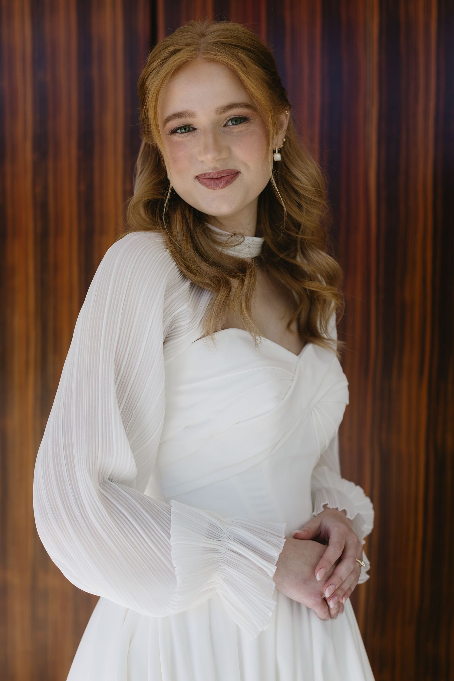 Elegant bridal portraits featuring white long-sleeved dress against warm toned background.