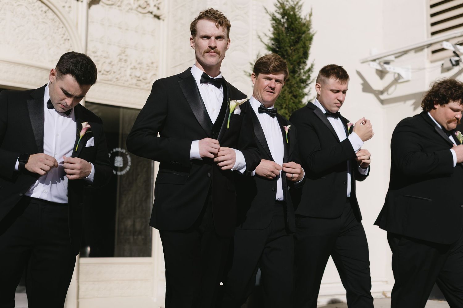 Groomsmen in black tuxedos gather for casual moment during wedding celebration.