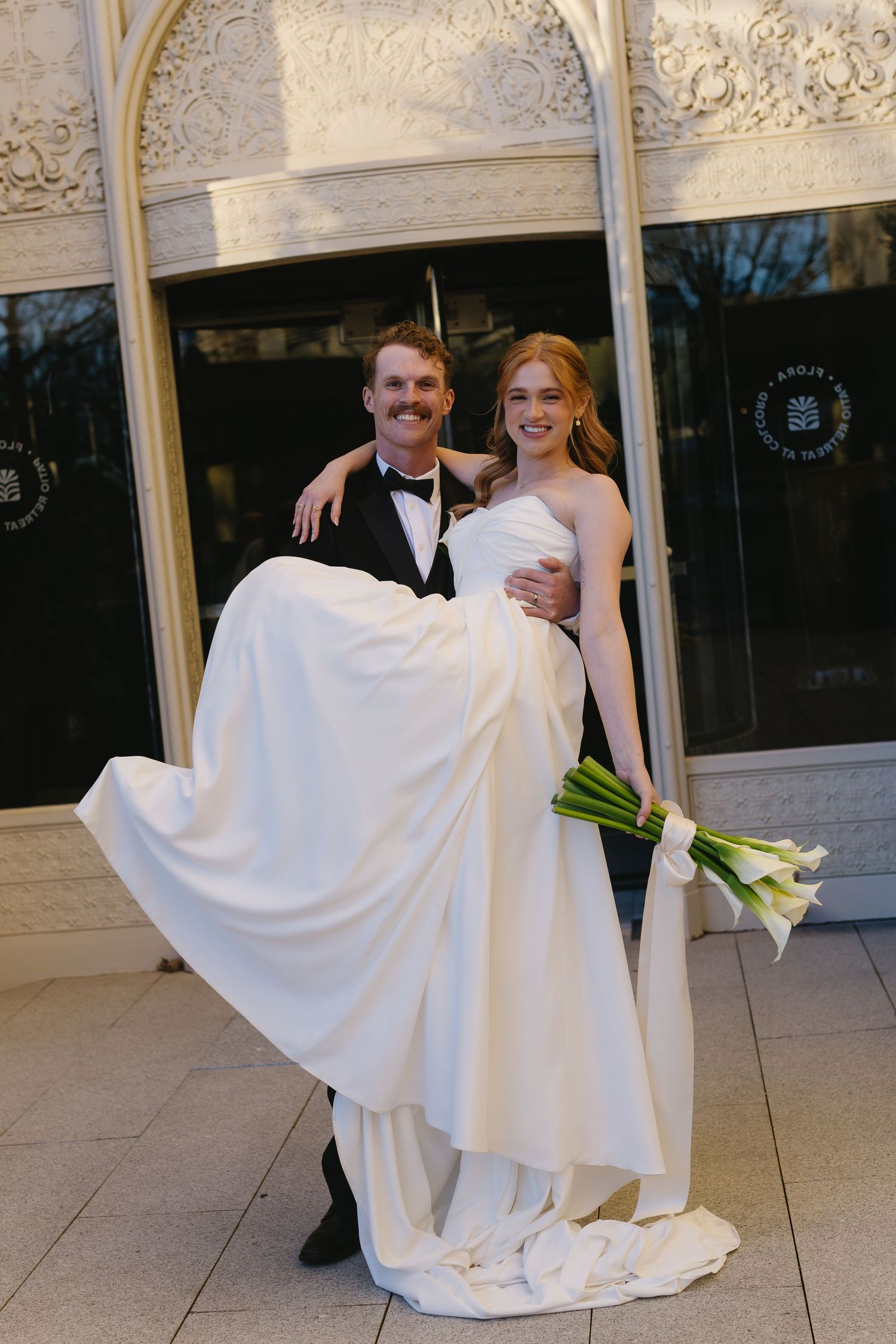 A couple dances playfully on an elegant patio with ornate stone walls and columns.